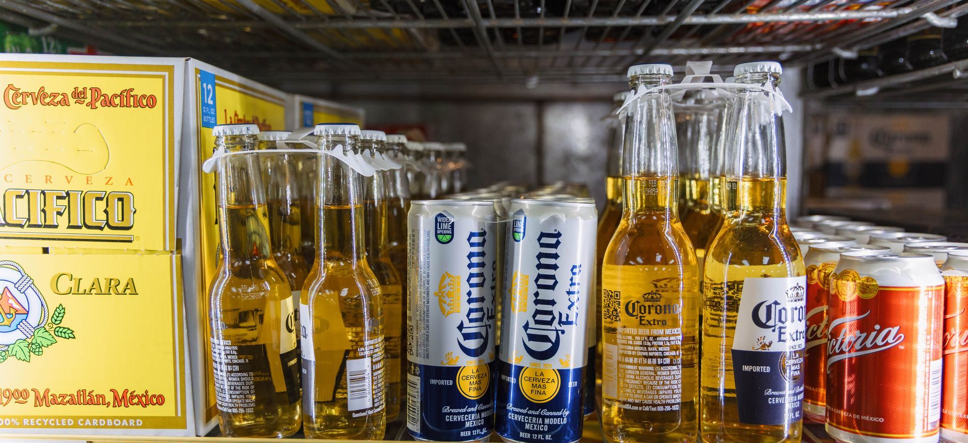 Bottles and cans of Corona beer inside a refrigerator. Some beers are boxed, behind the bottles.