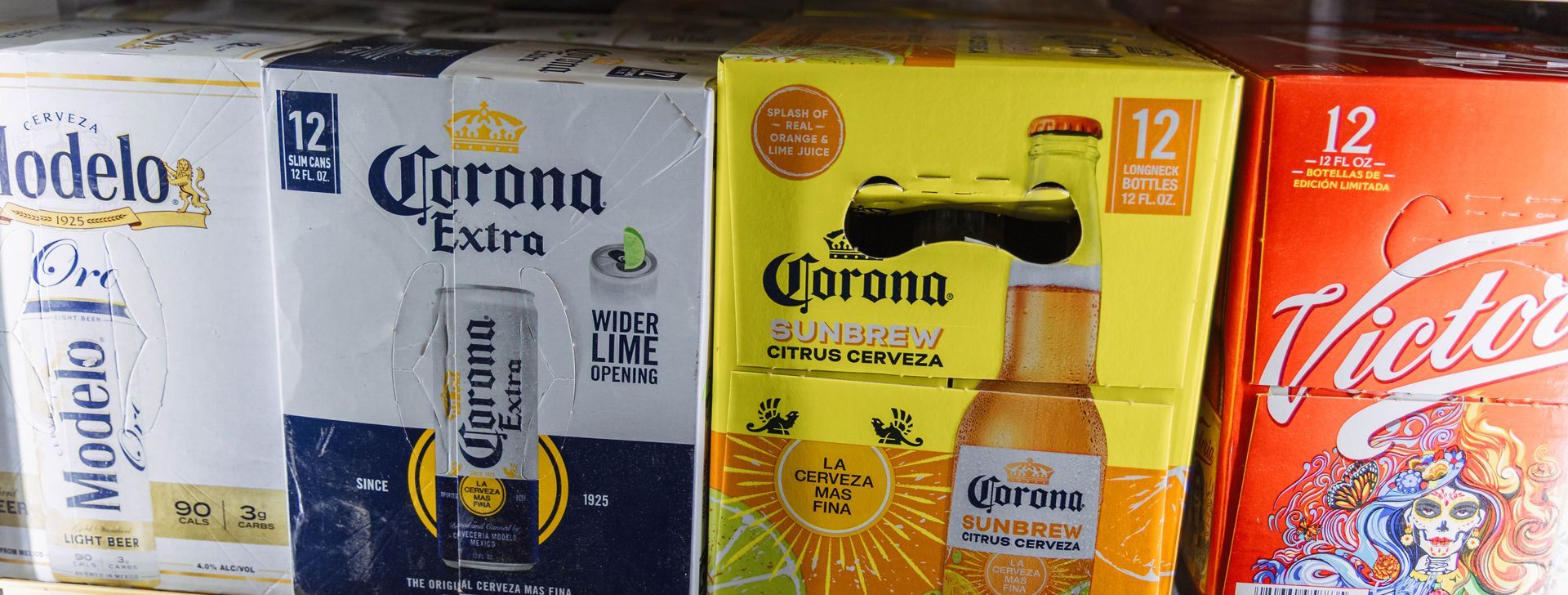 Beer boxes, Modelo, Corona Extra, Corona Light, and Victoria, on a shelf.