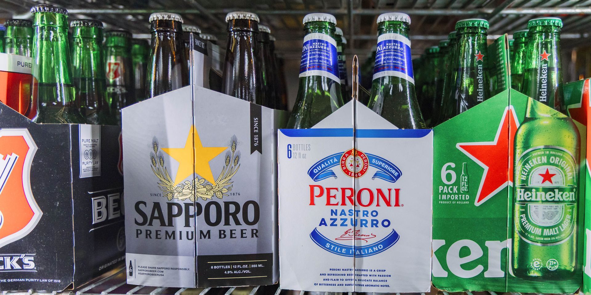 Close-up of various beer brands: Sapporo, Peroni, and Heineken in a refrigerated shelf.