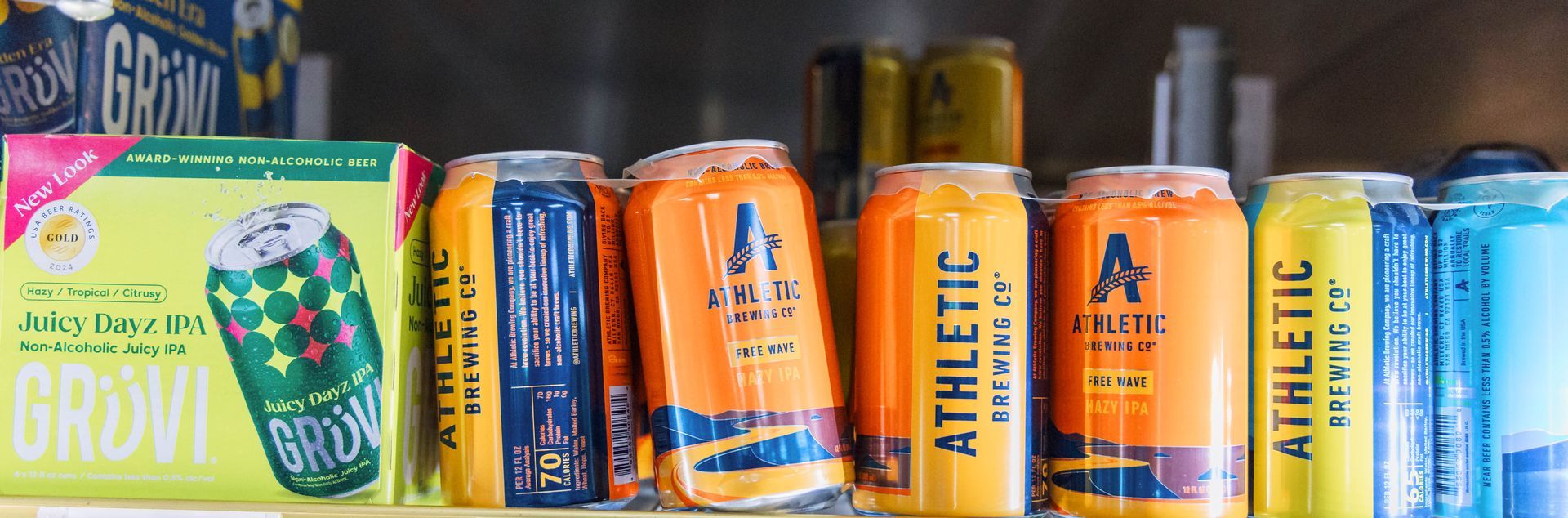 Canned beverages on a shelf. The cans are yellow, orange, blue, and green. The words