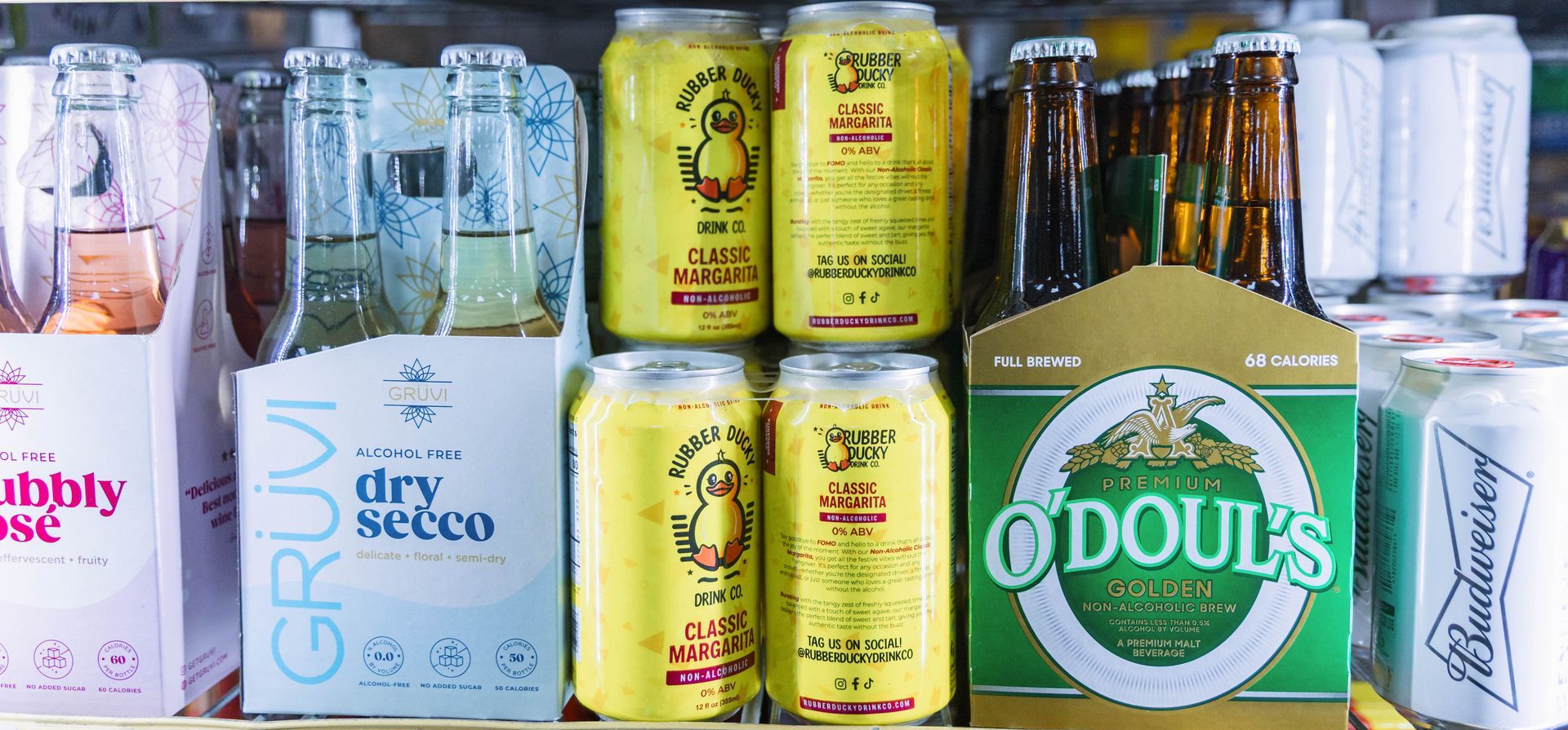 Shelf with alcoholic and non-alcoholic beverages: Sparkling wine, canned cocktails, beer bottles and cans.