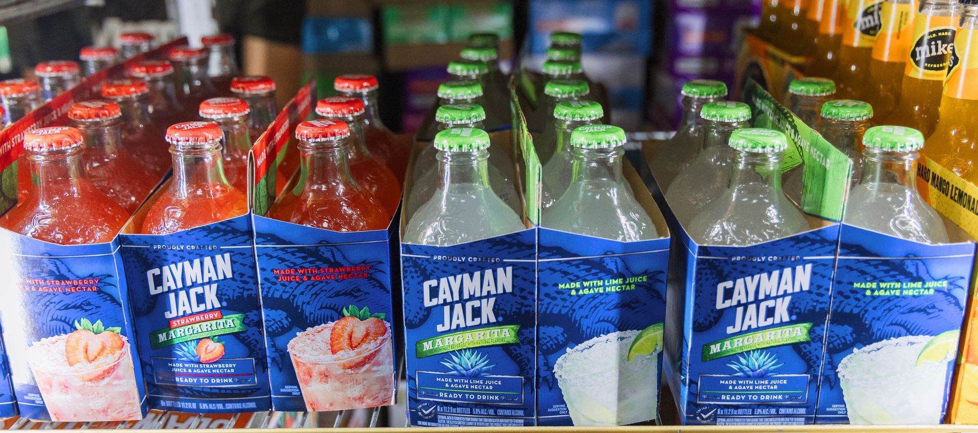 Bottled Cayman Jack drinks in a refrigerated display. Red-capped strawberry and green-capped margarita flavors.