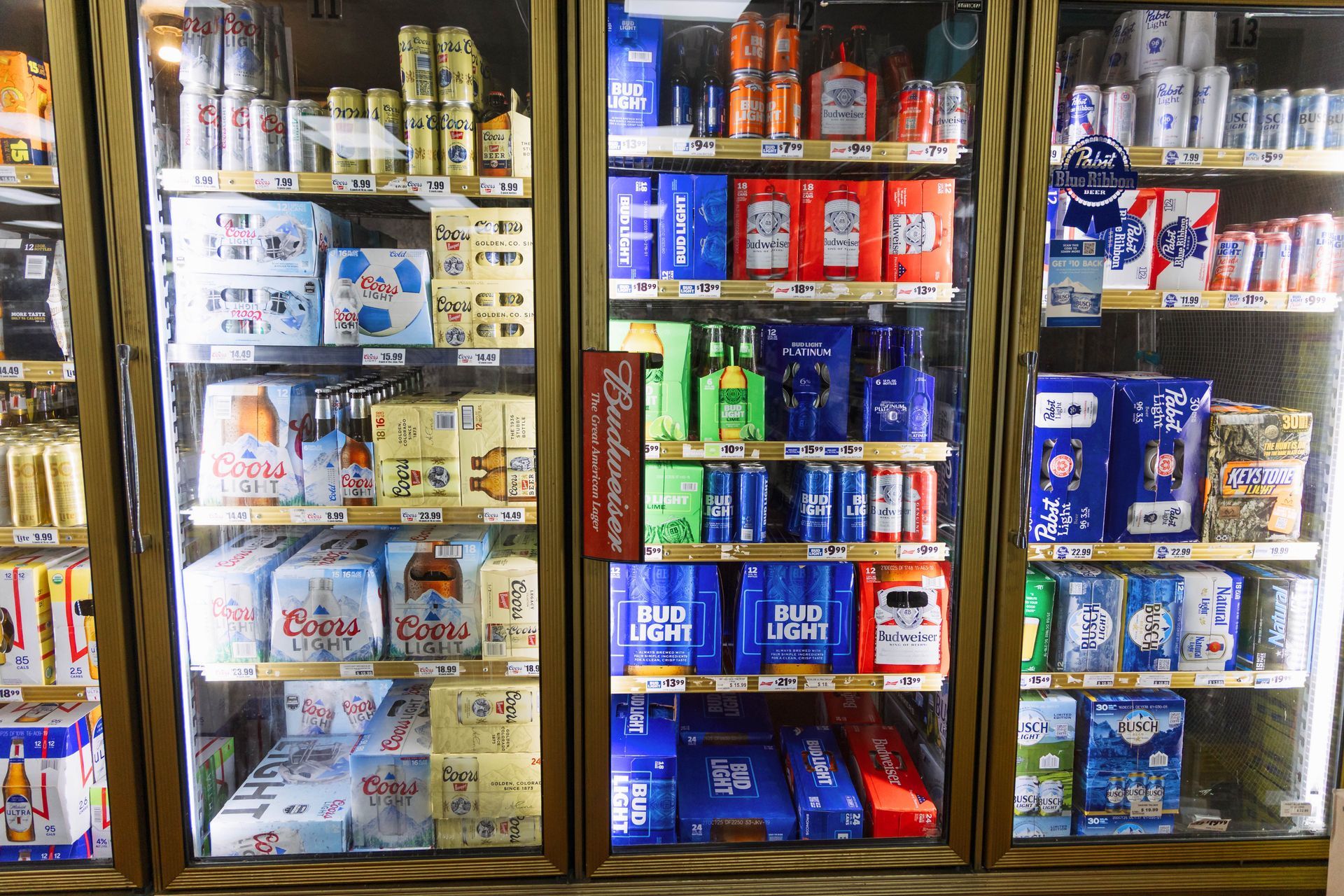 Refrigerated beer coolers in a store, filled with various brands of beer in cans and bottles.
