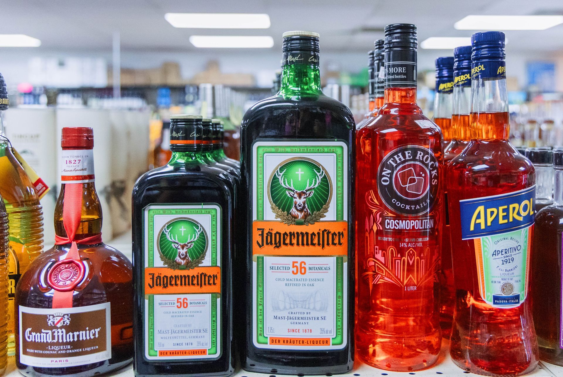 Bottles of assorted alcoholic beverages, including Jägermeister and Aperol, on a store shelf.