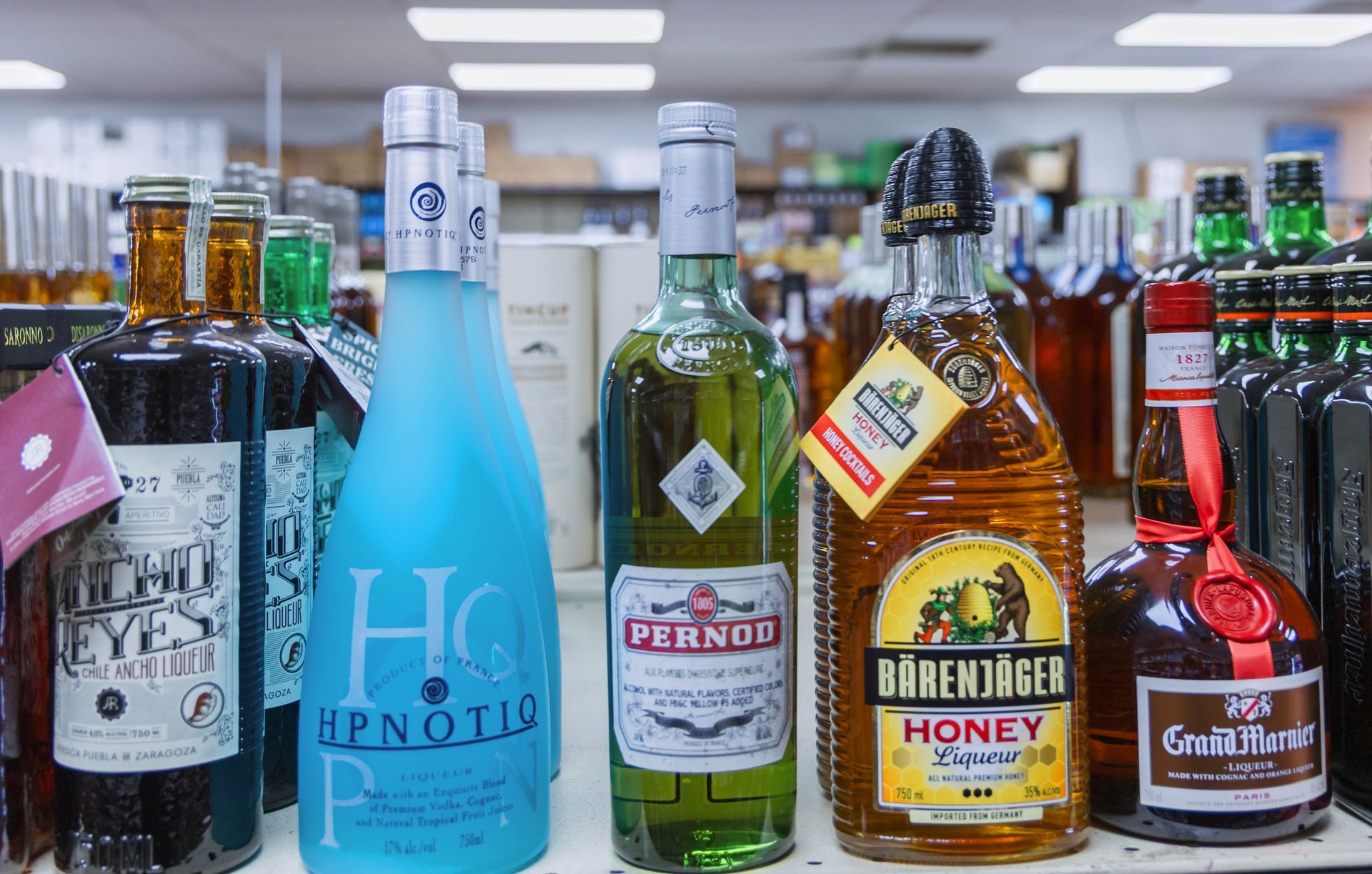 Liquor bottles on a store shelf: blue, green, yellow, and red bottles.