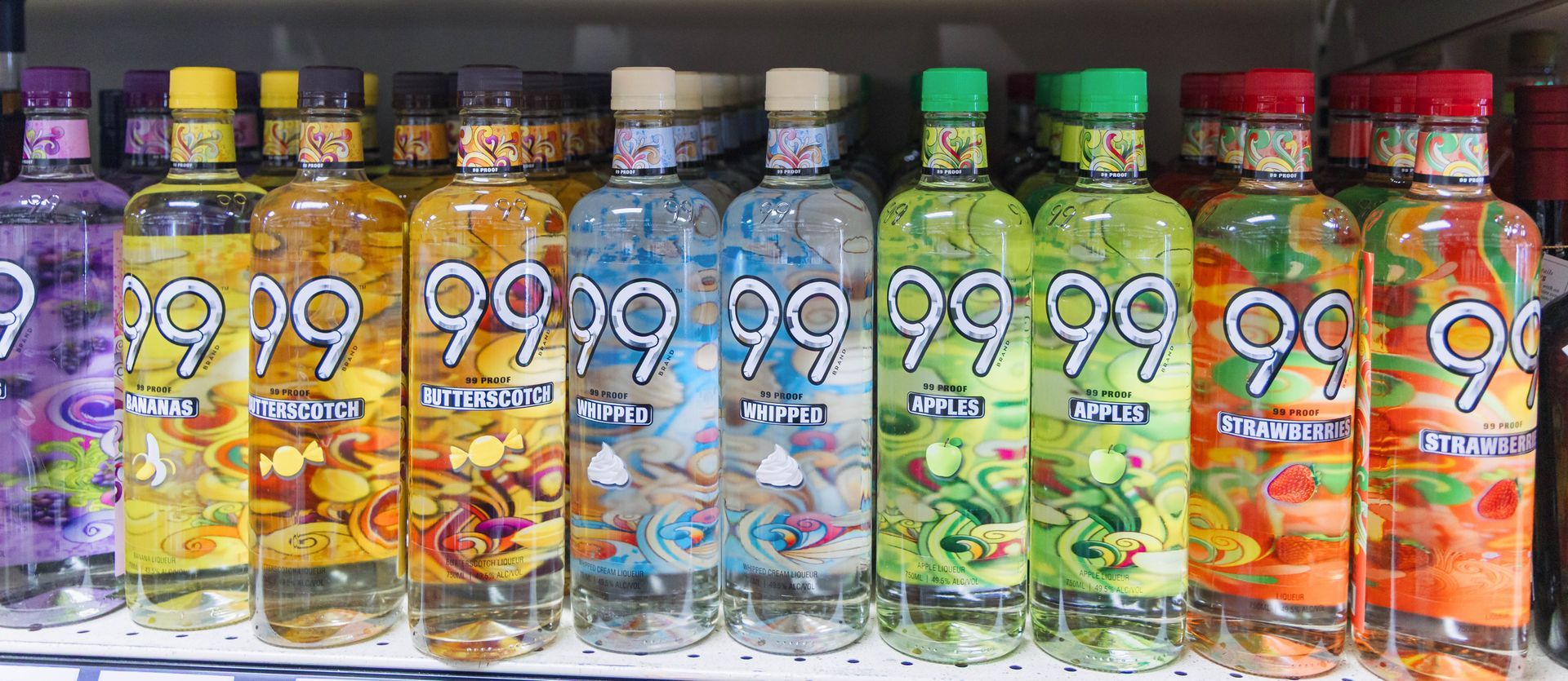 Bottles of liqueur with colorful labels, arranged on a shelf. The labels have the number