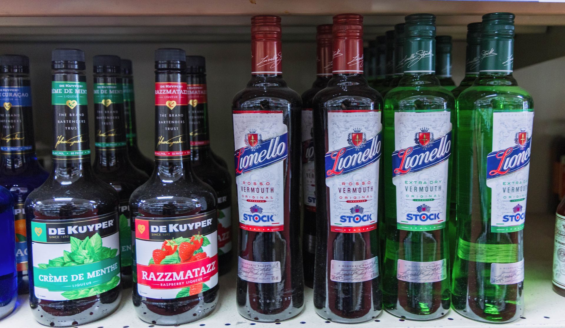 Bottles of liquor on a shelf: blue, green, black, and red. Labels vary, one says 'Stock'.