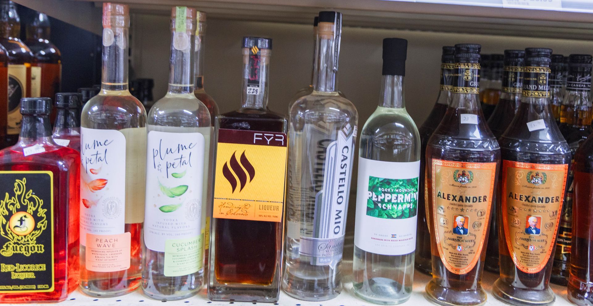 Liquor bottles on a shelf, various sizes, colors, and label designs, viewed indoors.