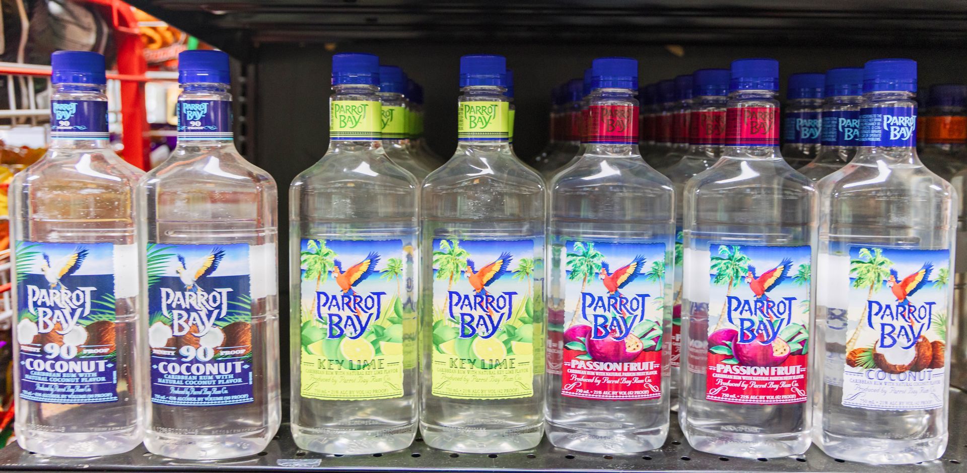 Bottles of Parrot Bay rum in various flavors on a shelf. Clear bottles with blue and color-coded labels.