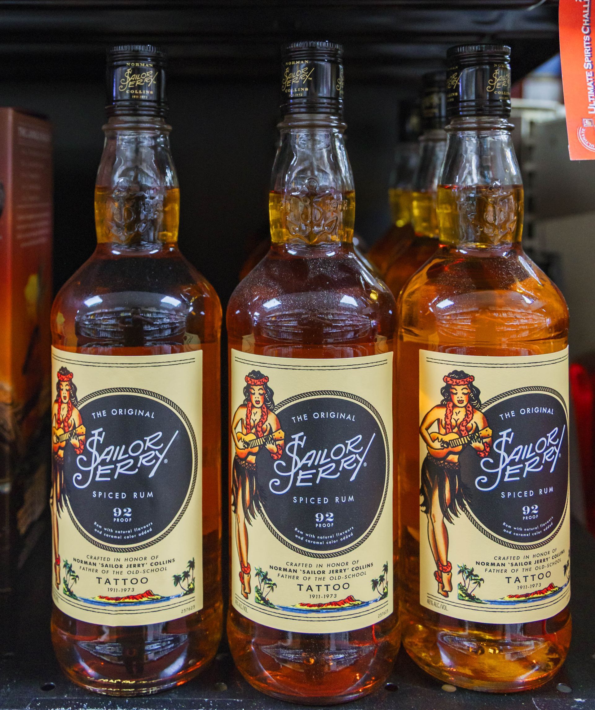 Three bottles of Sailor Jerry spiced rum on a shelf, each with a woman tattoo label.