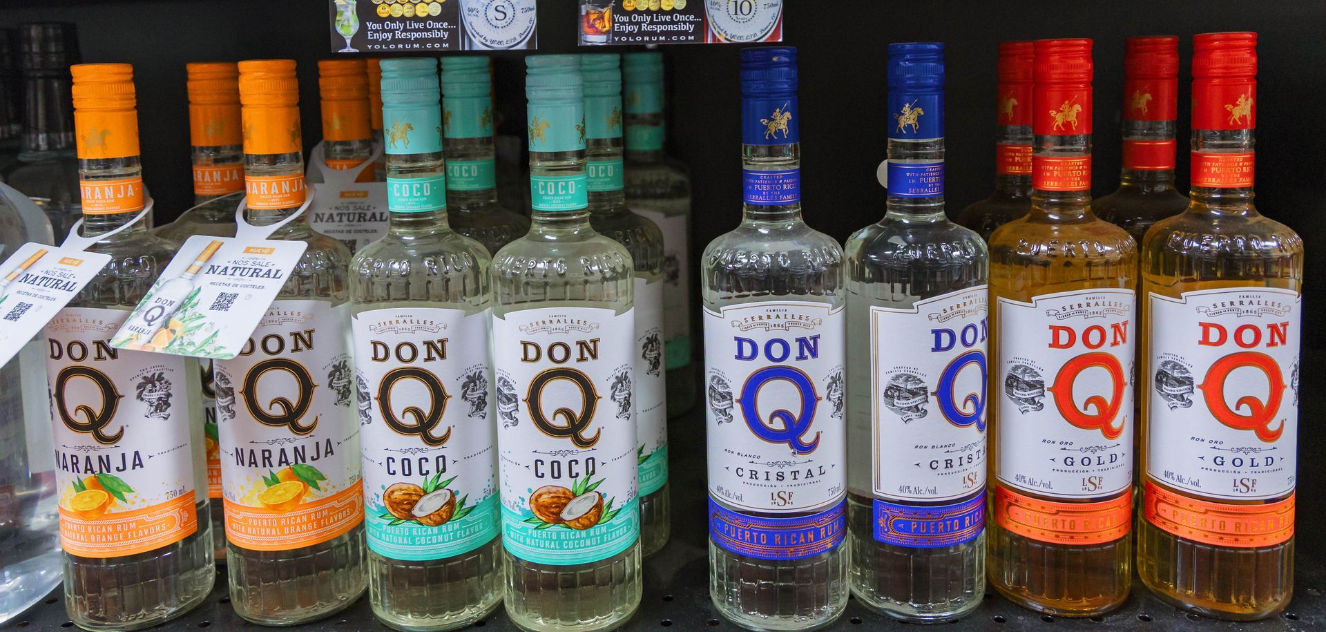 Bottles of Don Q rum with different colored labels and caps on a shelf.