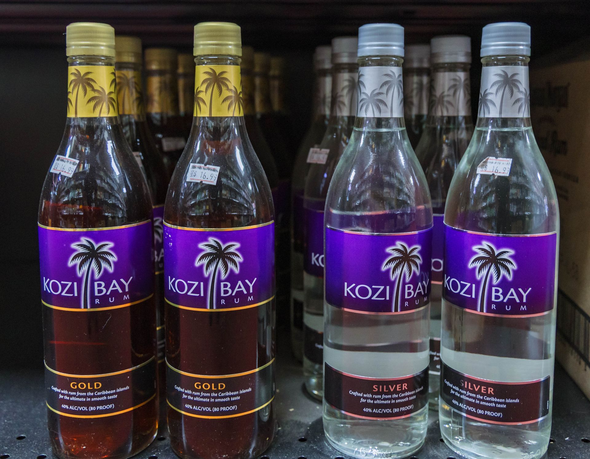 Bottles of Kozi Bay rum, gold and silver, with purple labels, on a store shelf.