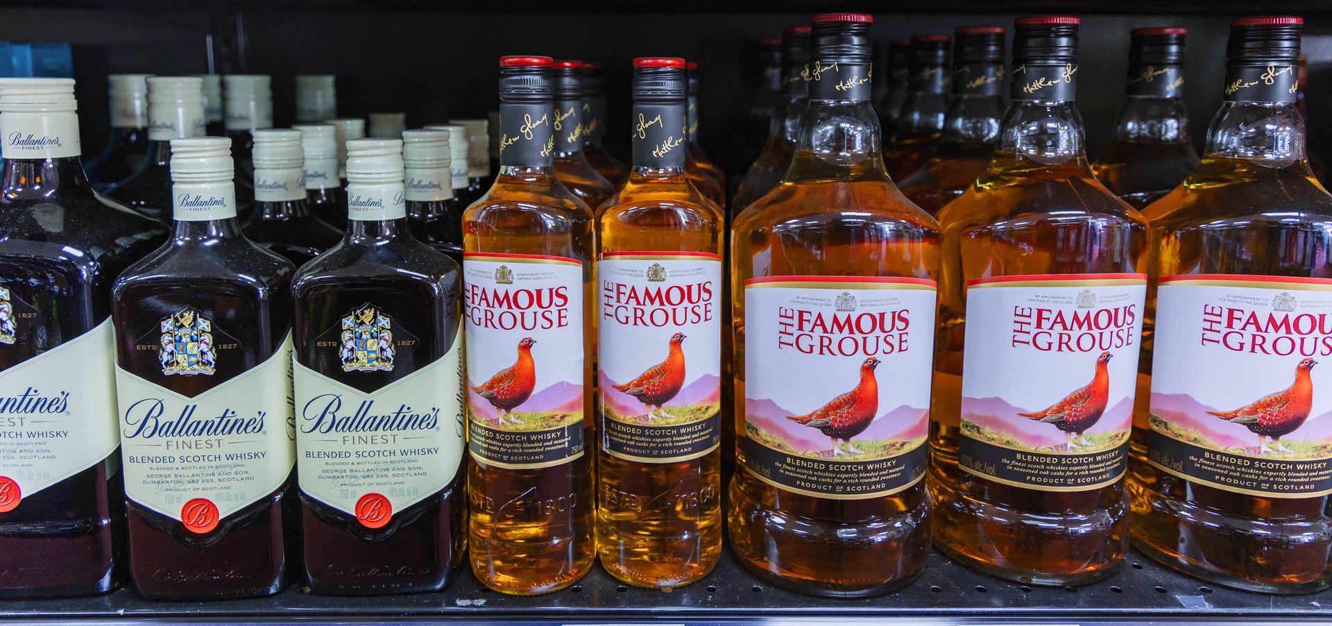 Bottles of liquor on a shelf, including Famous Grouse and Ballantine's.