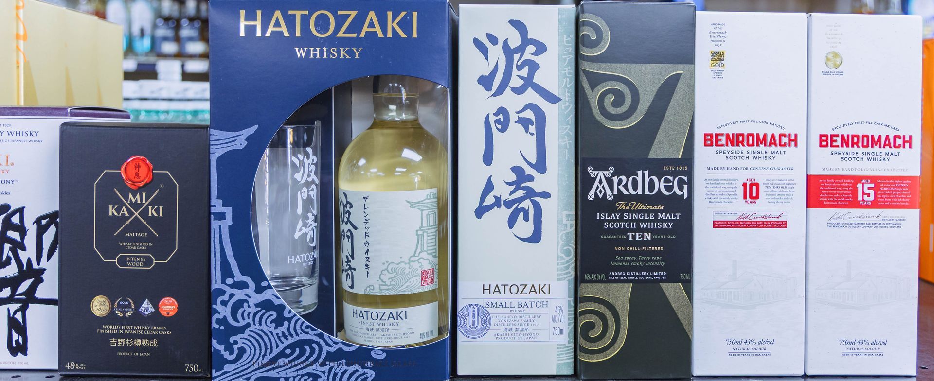 Row of liquor boxes: Japanese whisky brands including Hatozaki, Tajima, and two bottles of Benromach.