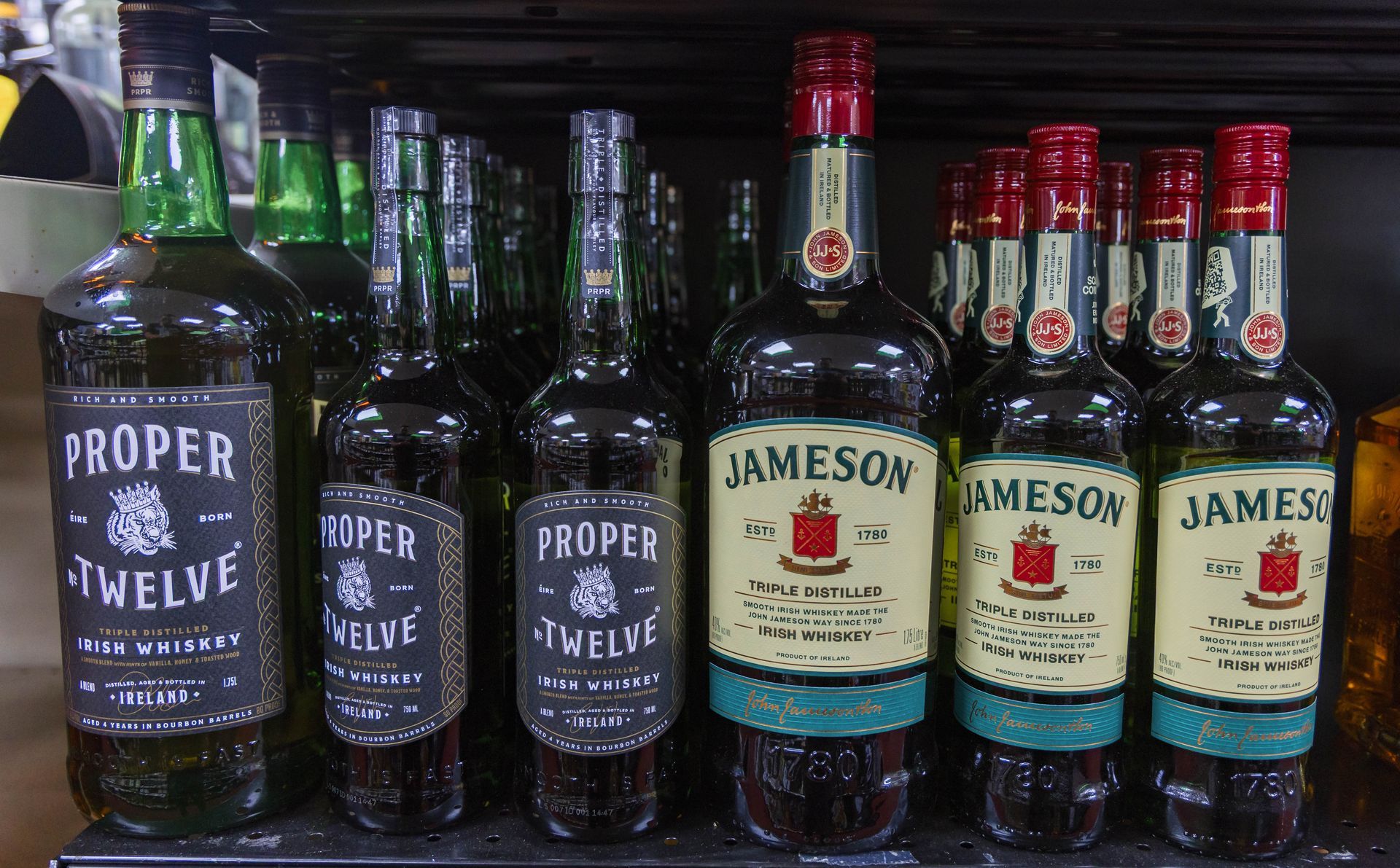 Bottles of Proper Twelve and Jameson Irish whiskey on a store shelf.