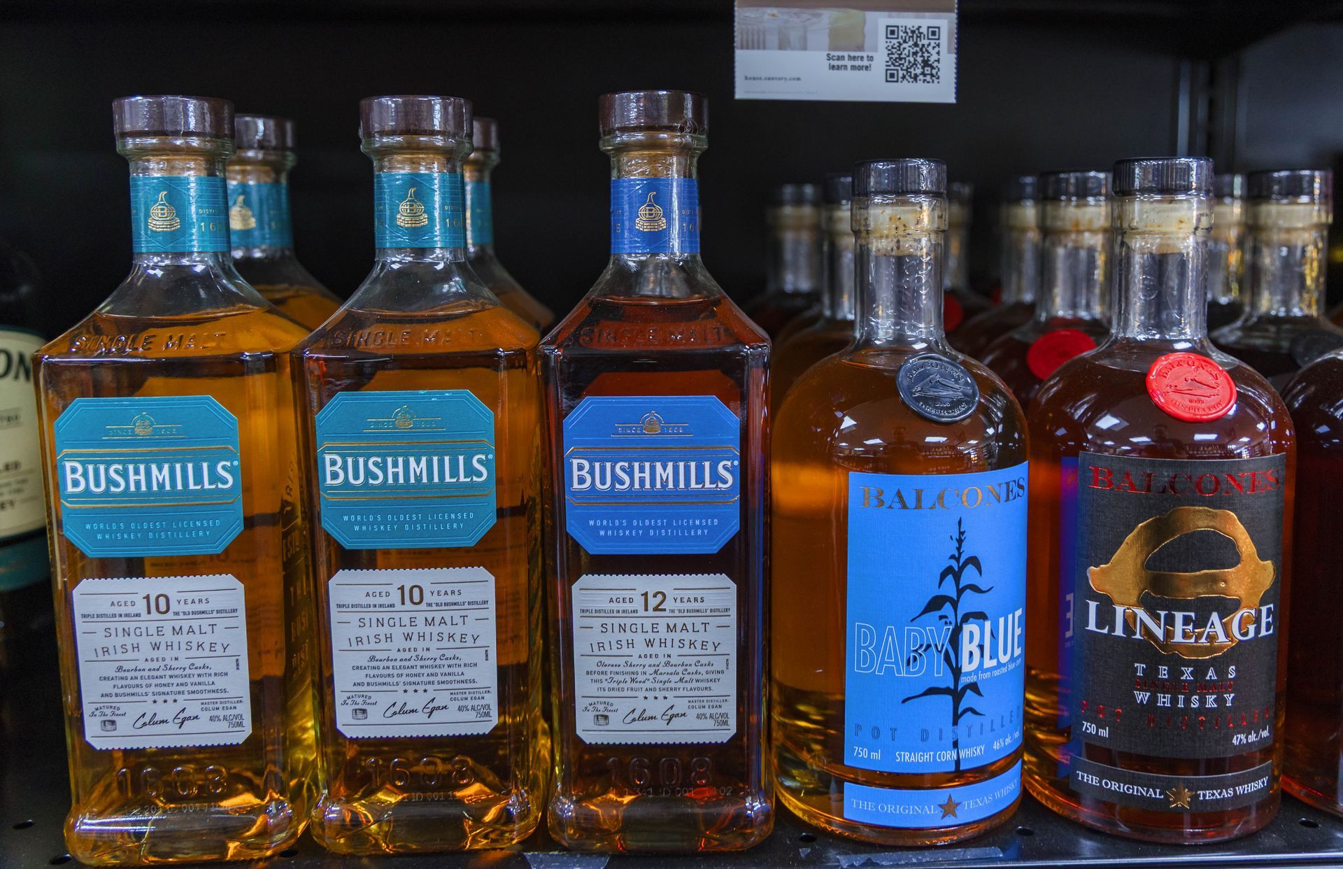 Bottles of Bushmills Irish Whiskey and other brands on a store shelf.