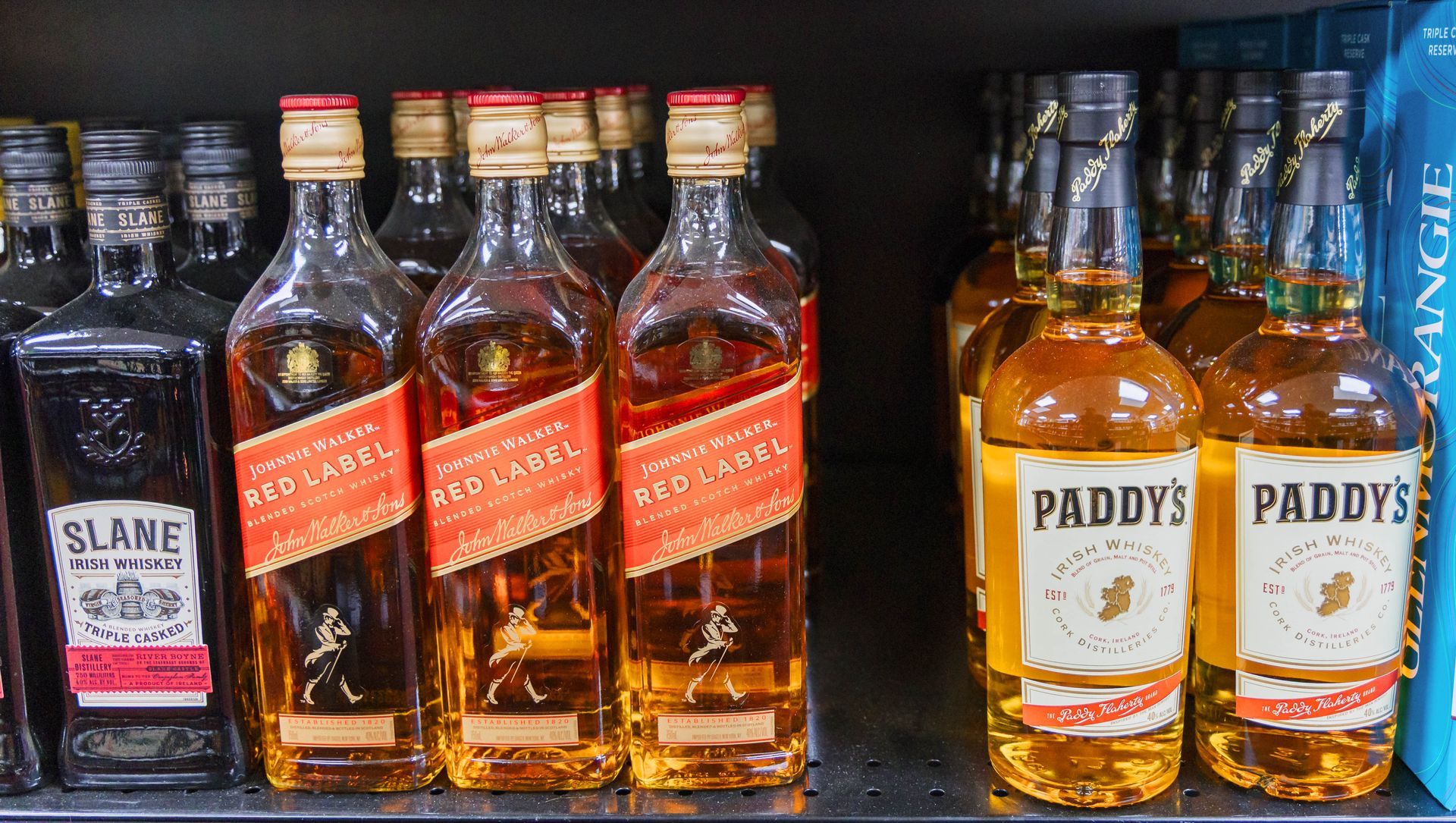 Shelves stocked with liquor bottles: Johnnie Walker Red Label, Paddy's, and Slane whiskey.