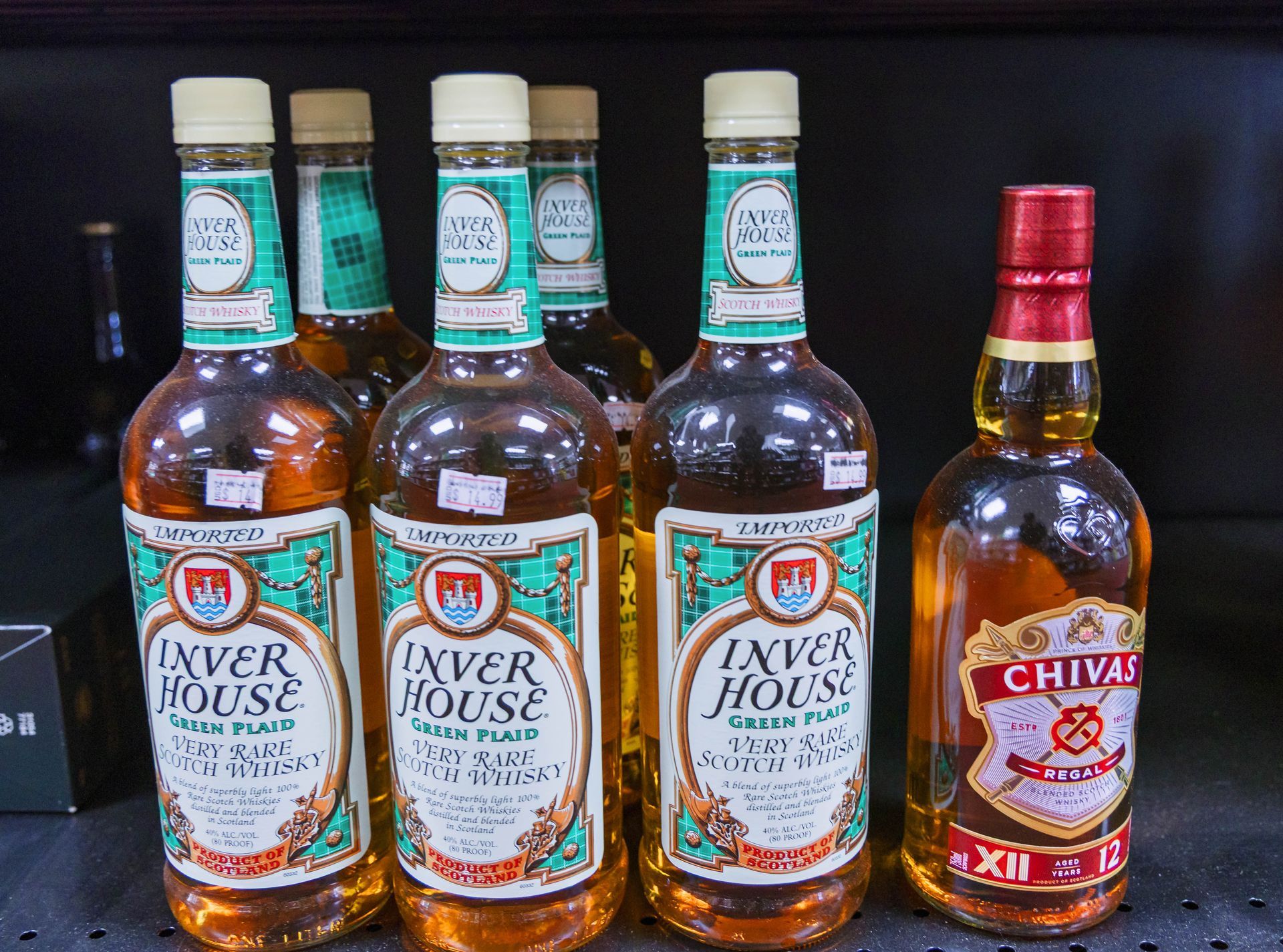 Bottles of whiskey for sale: Inver House Scotch with green labels and Chivas Regal with a red label.