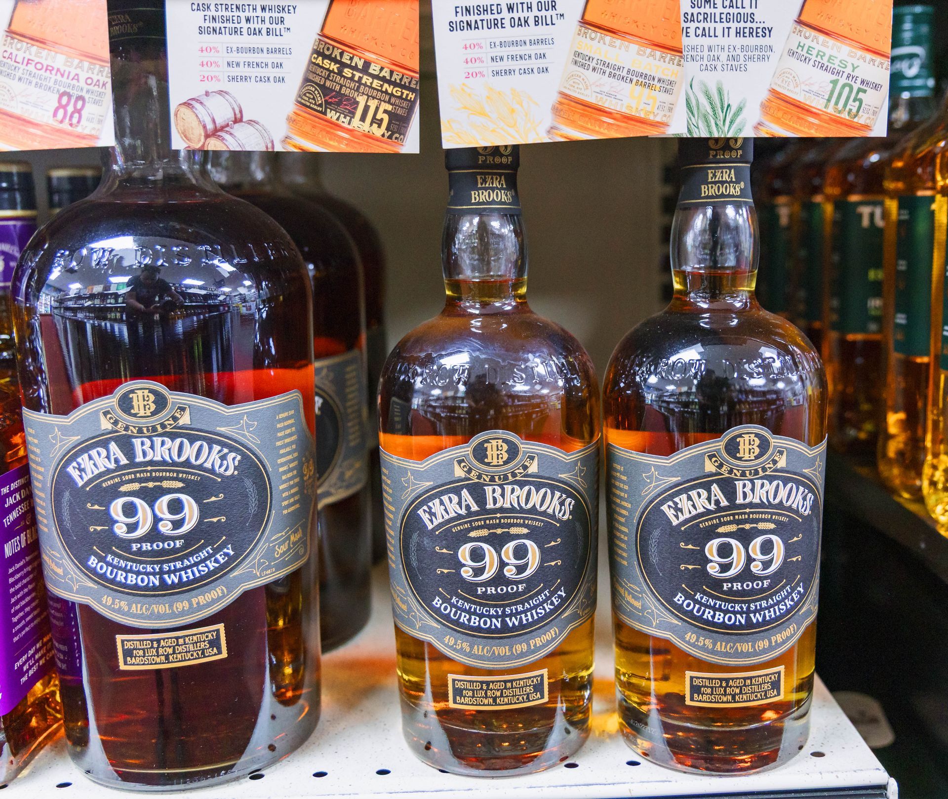 Three bottles of Ezra Brooks 99 bourbon whiskey on a store shelf, lit with warm lighting.