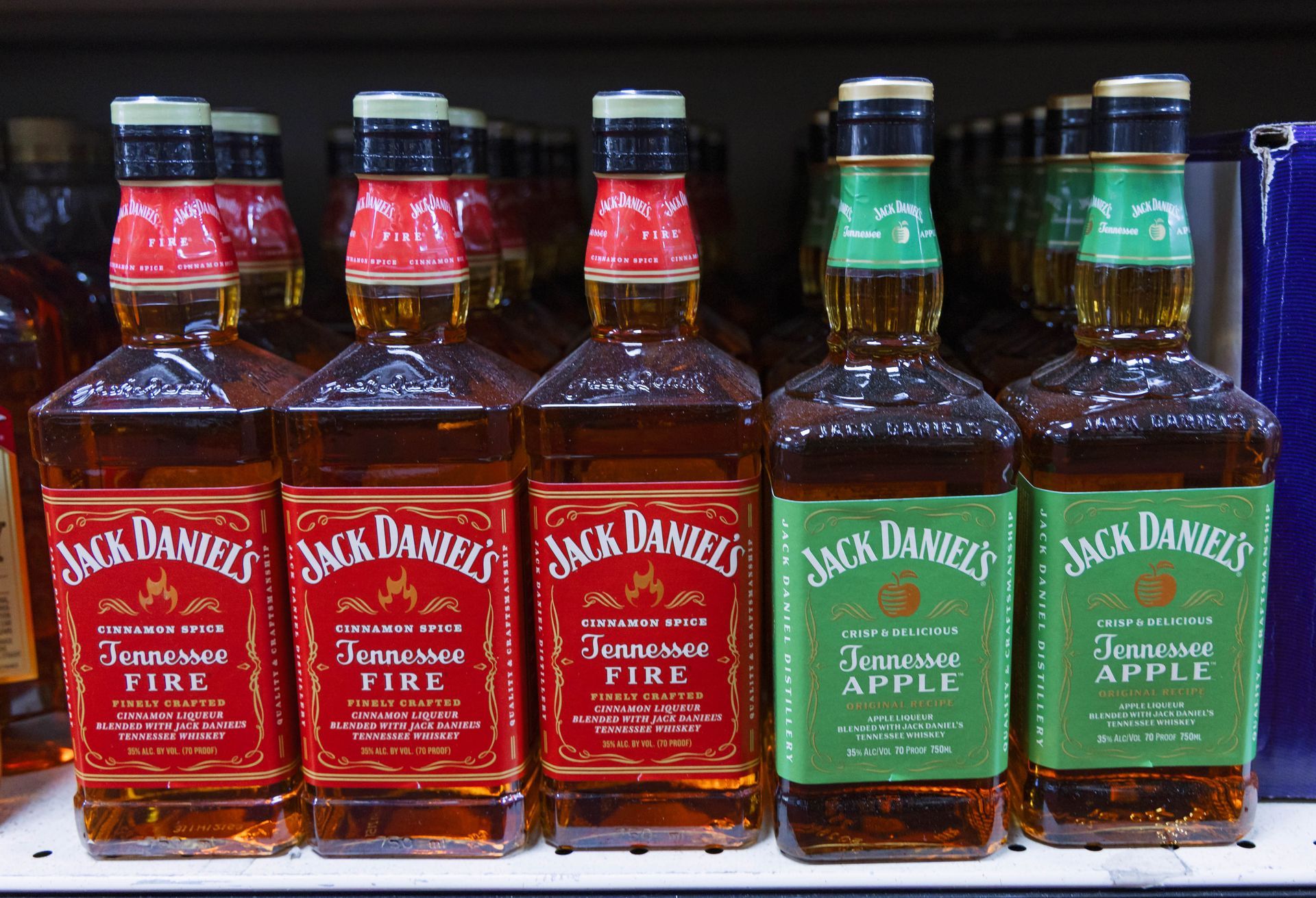 Bottles of Jack Daniel's Tennessee Fire and Tennessee Apple whiskey on a shelf, red and green labels visible.