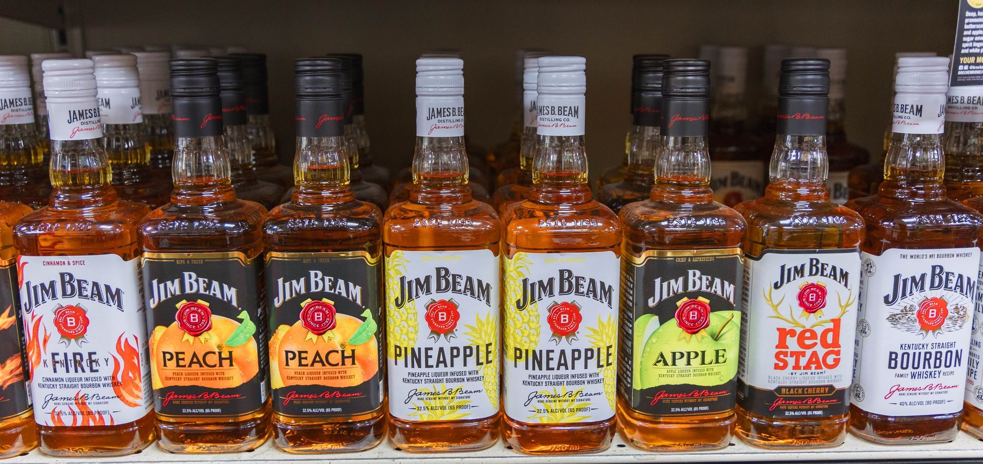 Shelves of Jim Beam flavored bourbon whiskey bottles, including peach, pineapple, apple, and red stag.