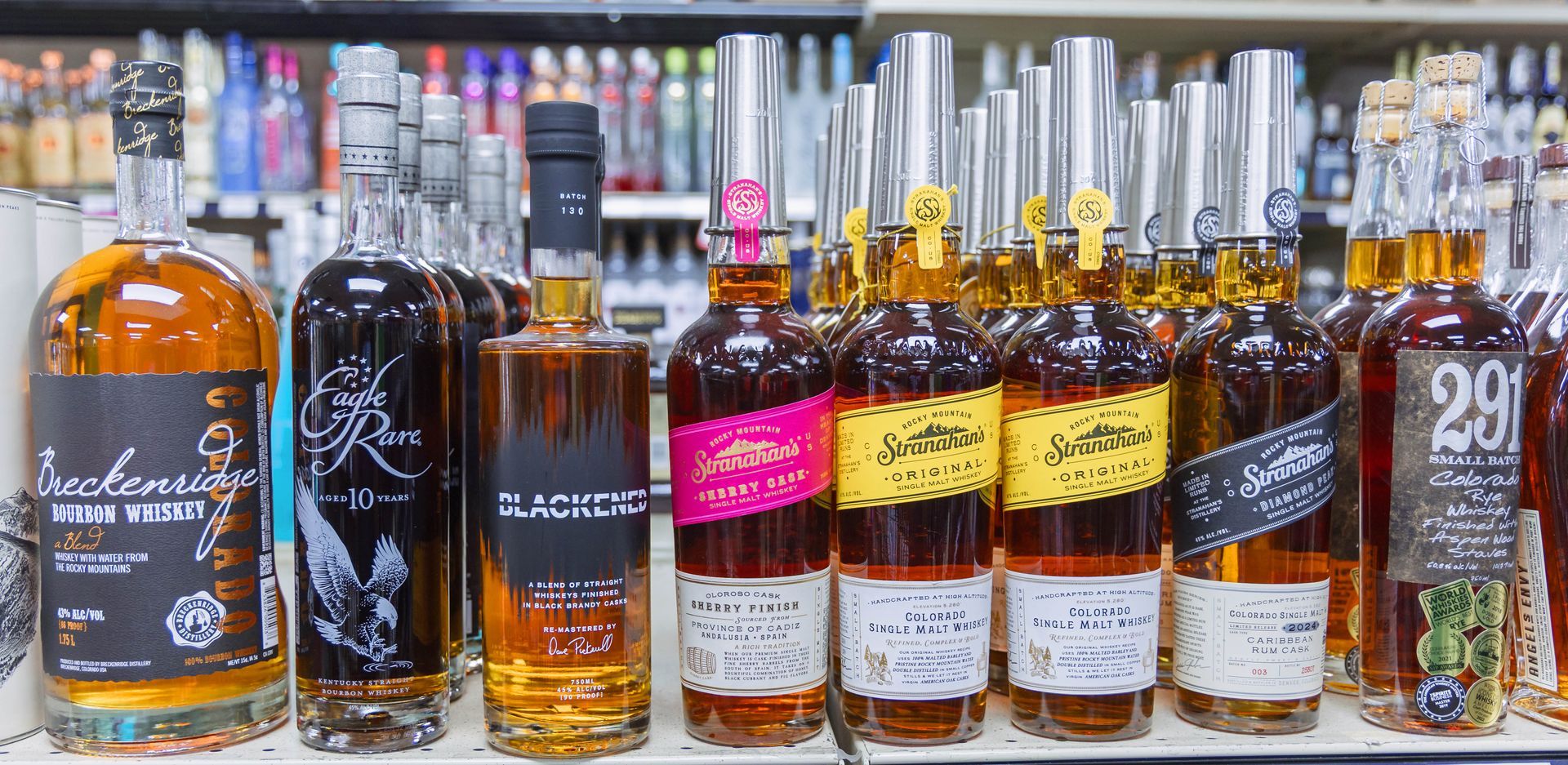 Bottles of liquor on a shelf, several with colorful labels, in a store setting.