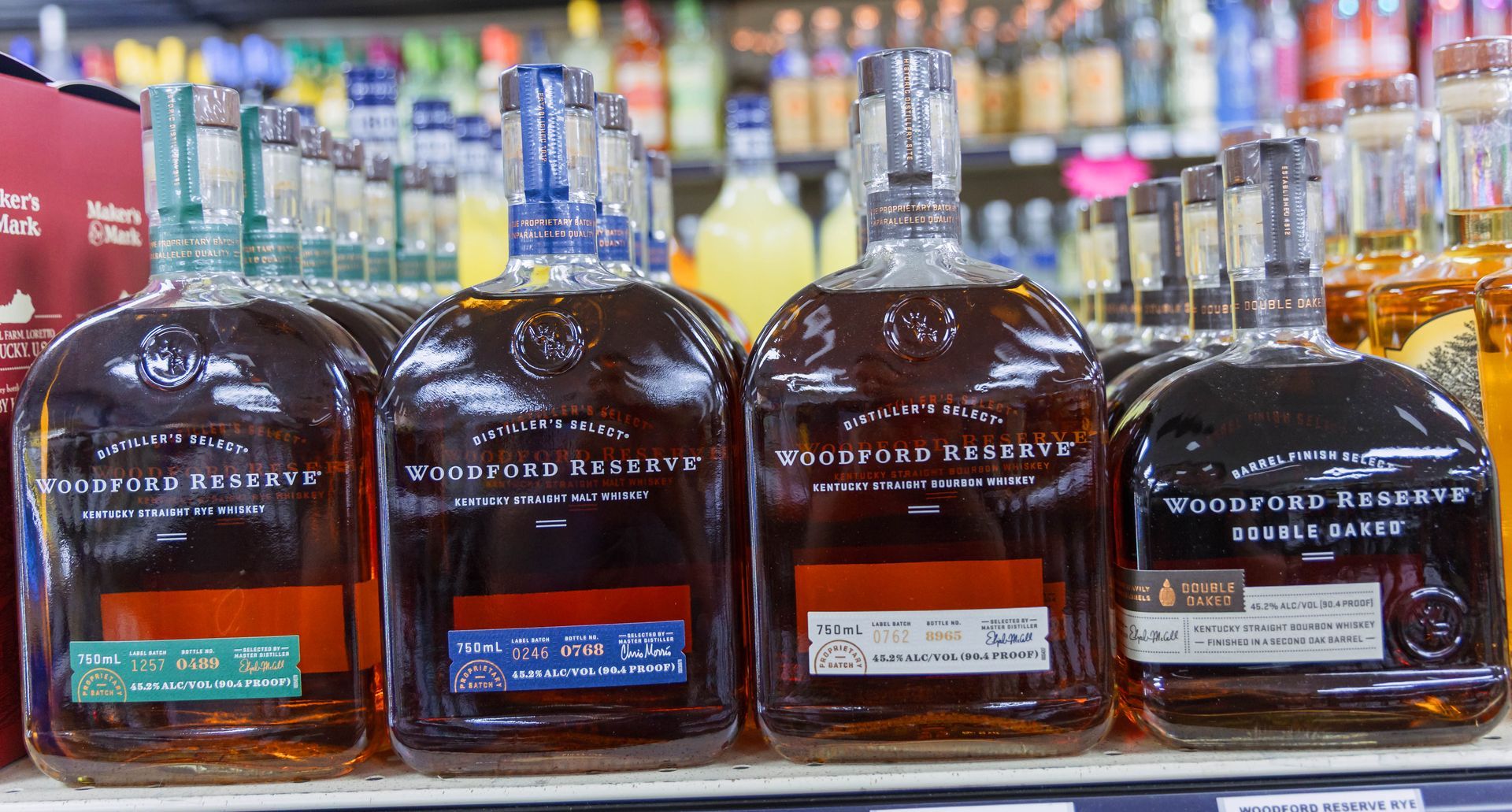 Four bottles of Woodford Reserve bourbon on a shelf, varying label colors.