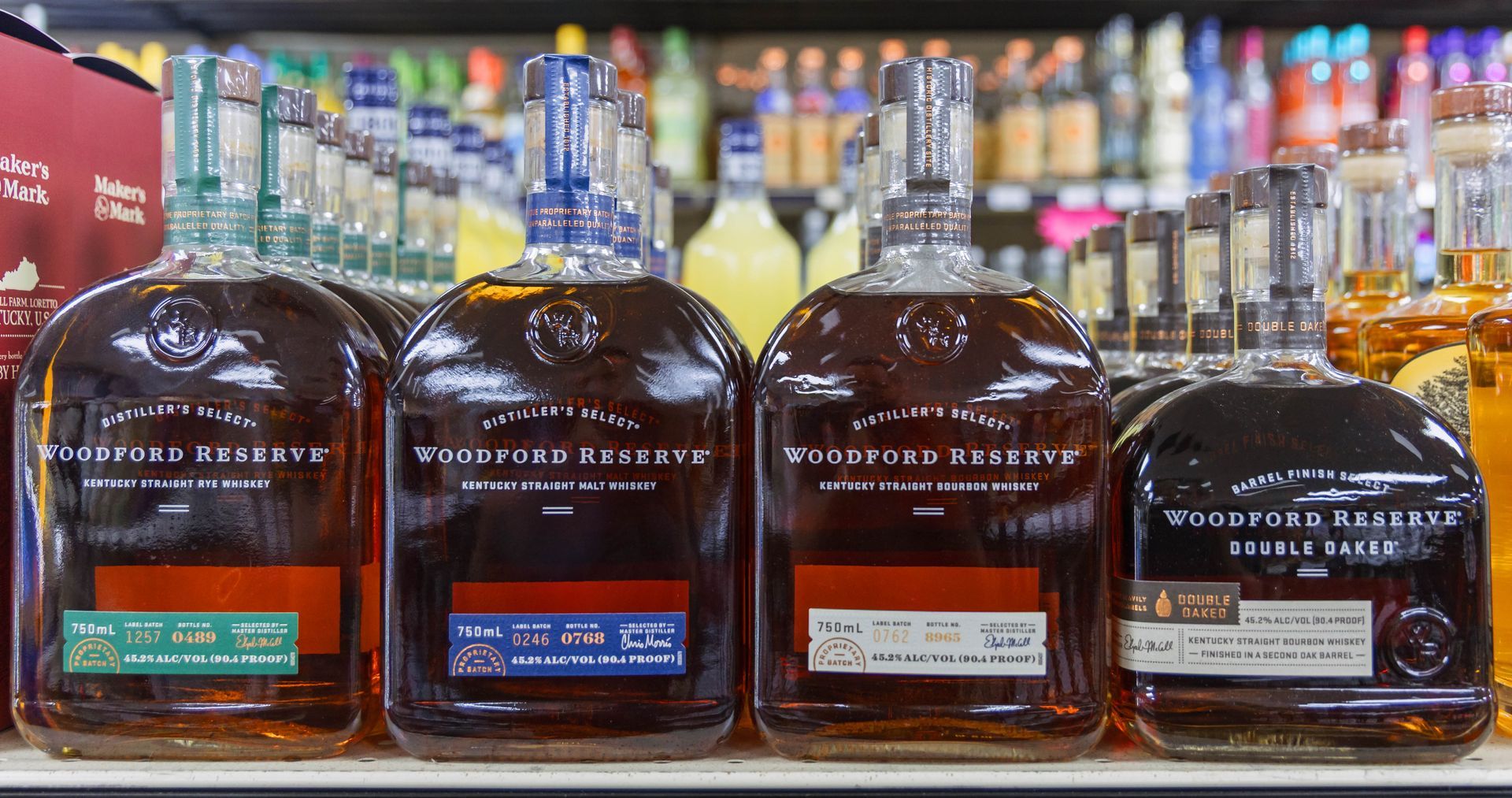 Four bottles of Woodford Reserve bourbon, with different label colors, on a shelf in a liquor store.