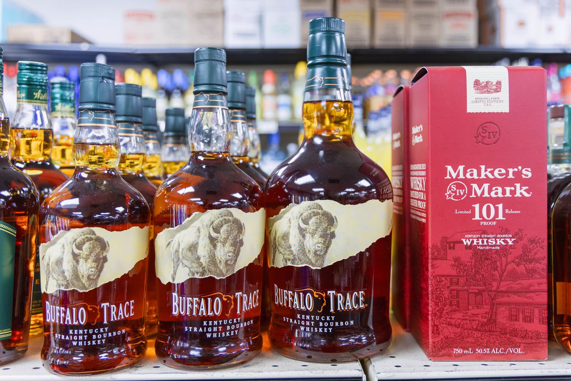 Bottles of Buffalo Trace whiskey and a box of Maker's Mark 101 whiskey on a store shelf.