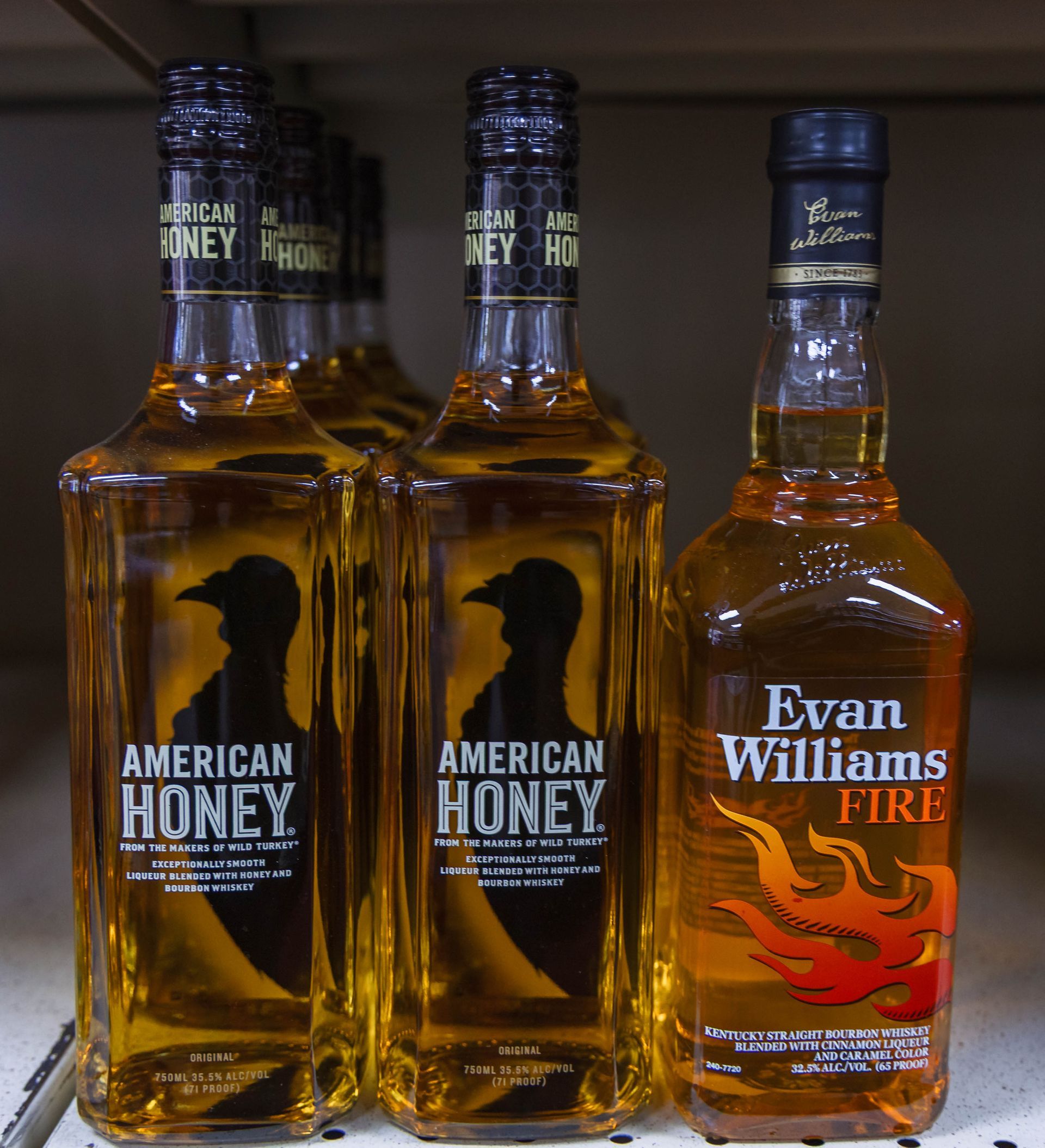 Bottles of American Honey and Evan Williams Fire whiskey on a shelf, amber liquid, black labels.