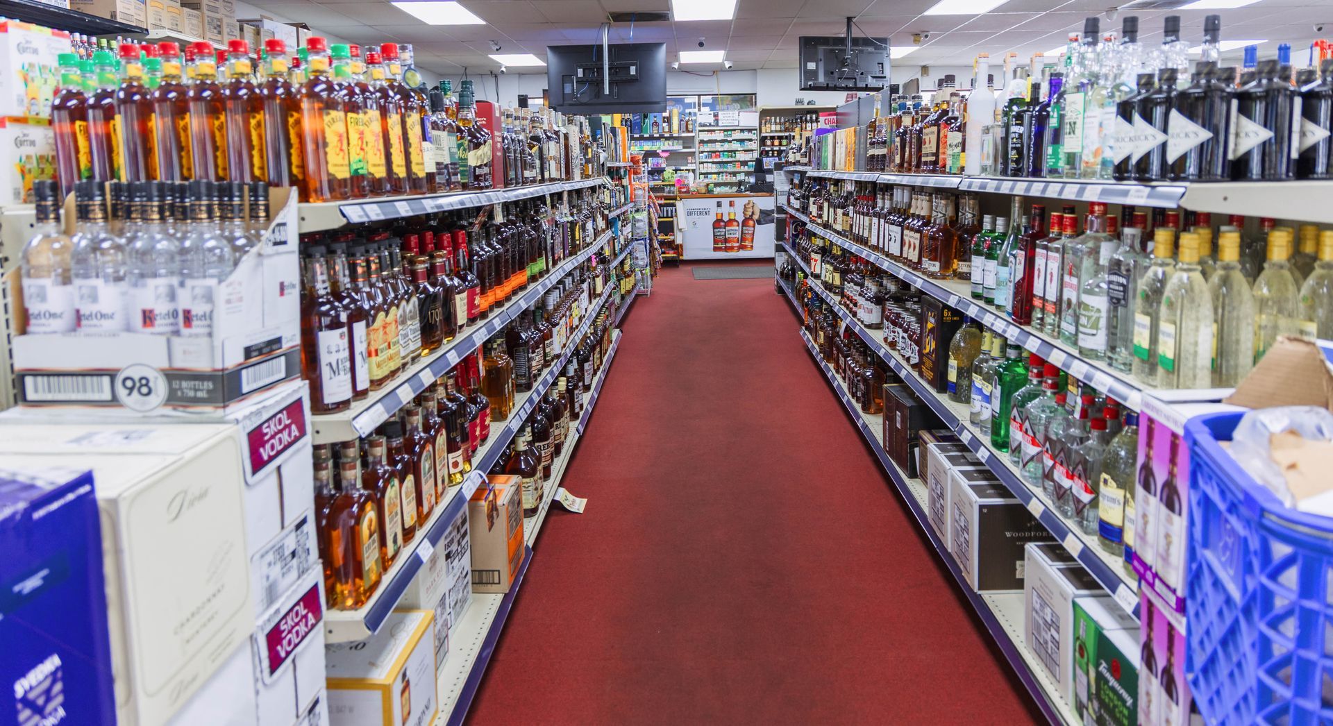 Liquor store aisle with shelves of bottles, red carpet, bright lights.