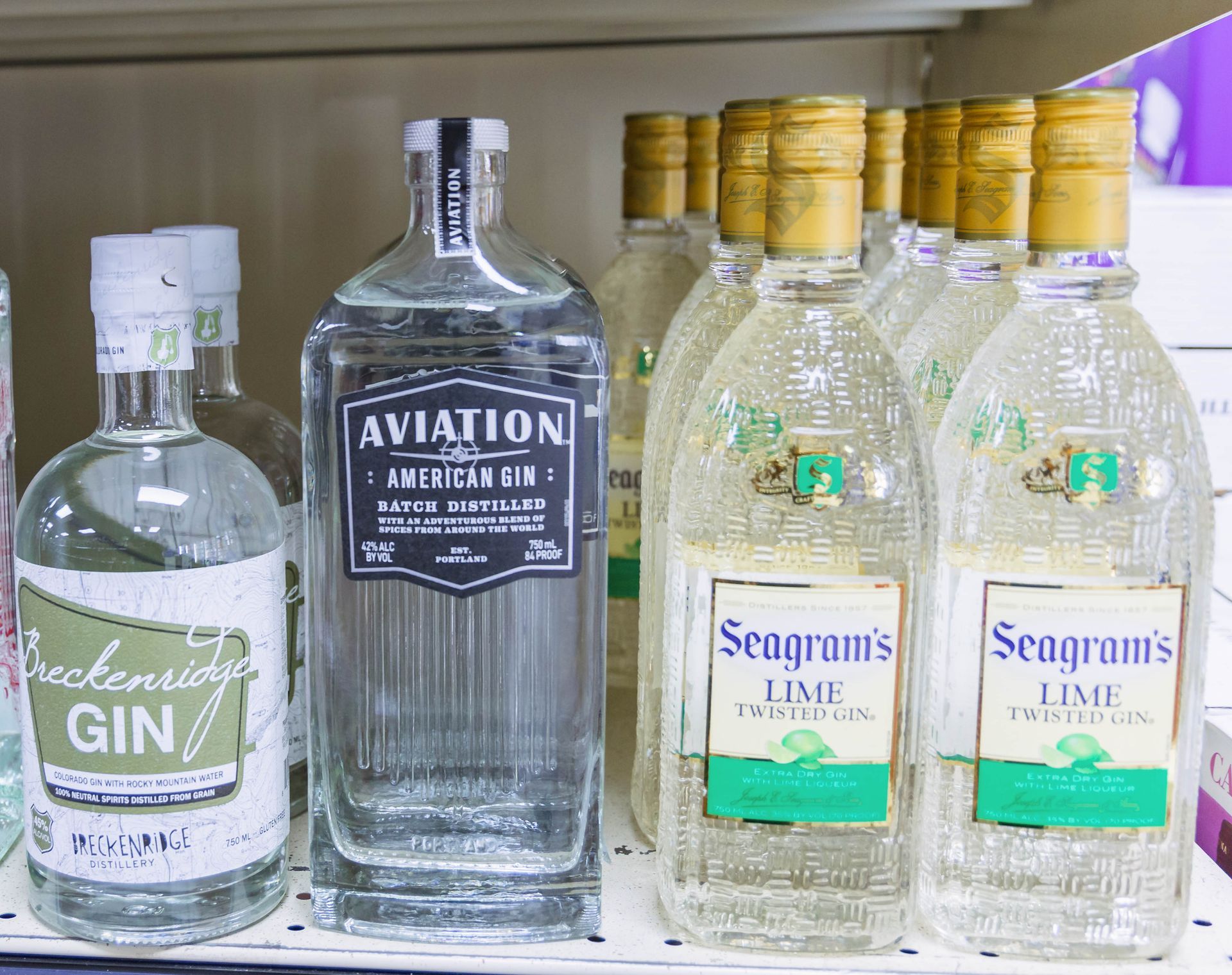Bottles of gin on a shelf, including Aviation, Breckenridge, and Seagram's Lime Twisted.
