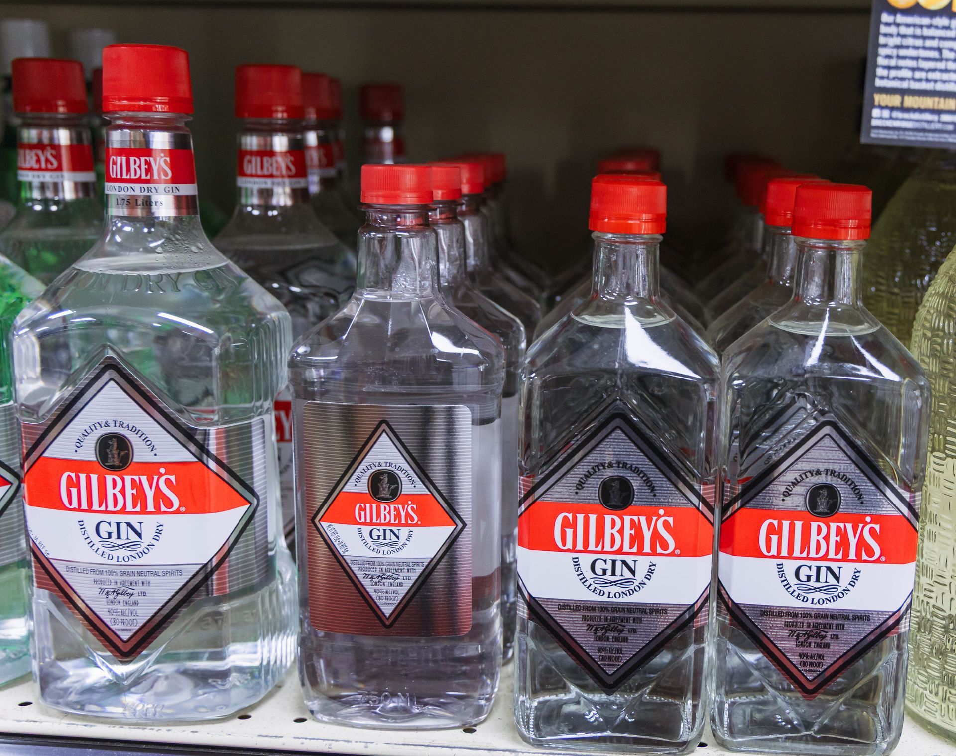 Gilbey's gin bottles with red caps, on a shelf, labeled with a red and white diamond.