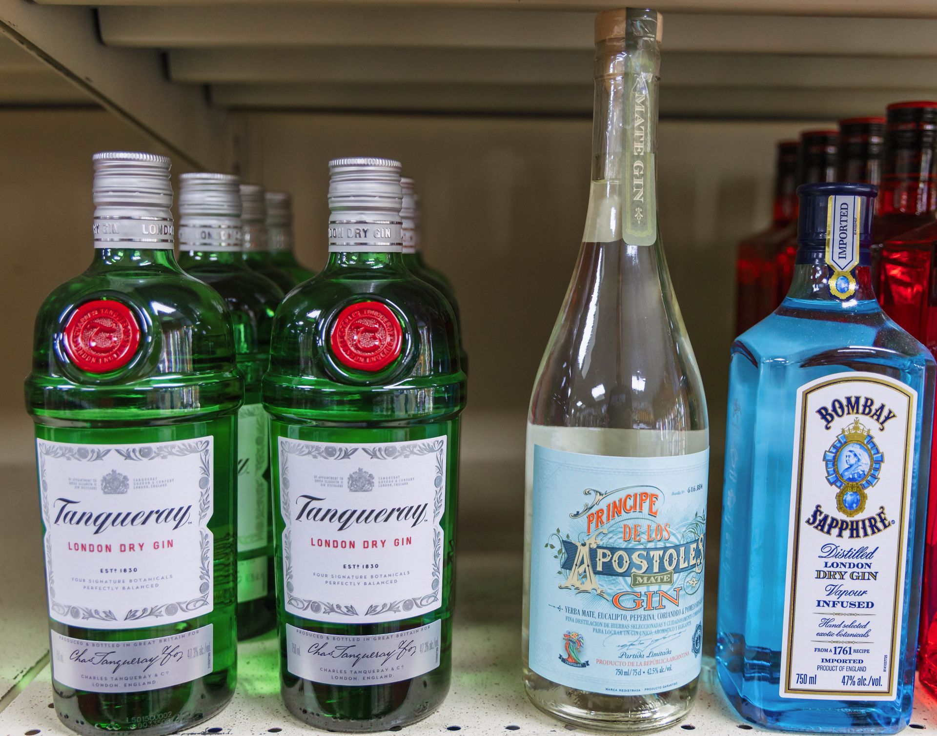 Bottles of gin on a shelf, including green Tanqueray, clear Postol, and blue Bombay Sapphire.