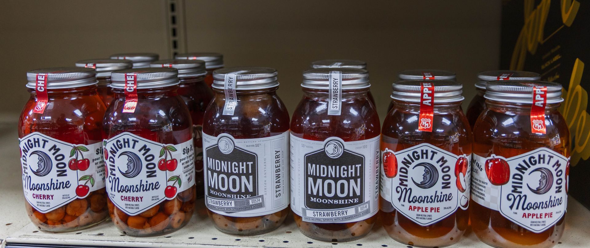 Jars of Midnight Moon Moonshine on a shelf, various flavors visible with colorful fruits.