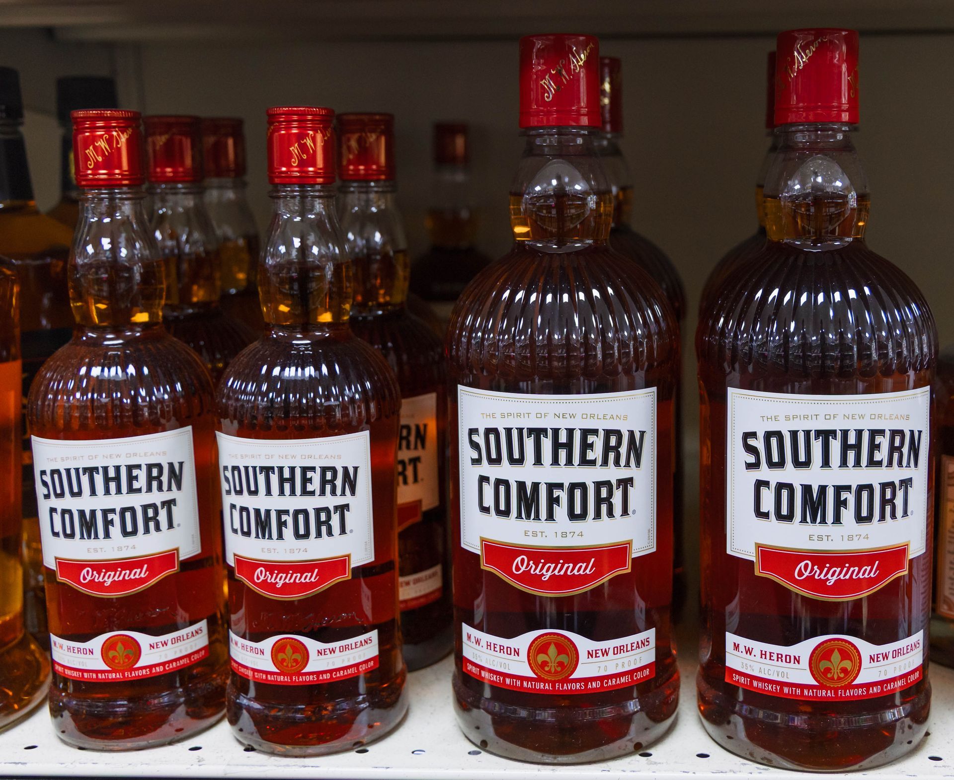 Bottles of Southern Comfort liquor with red caps and white labels on a shelf.