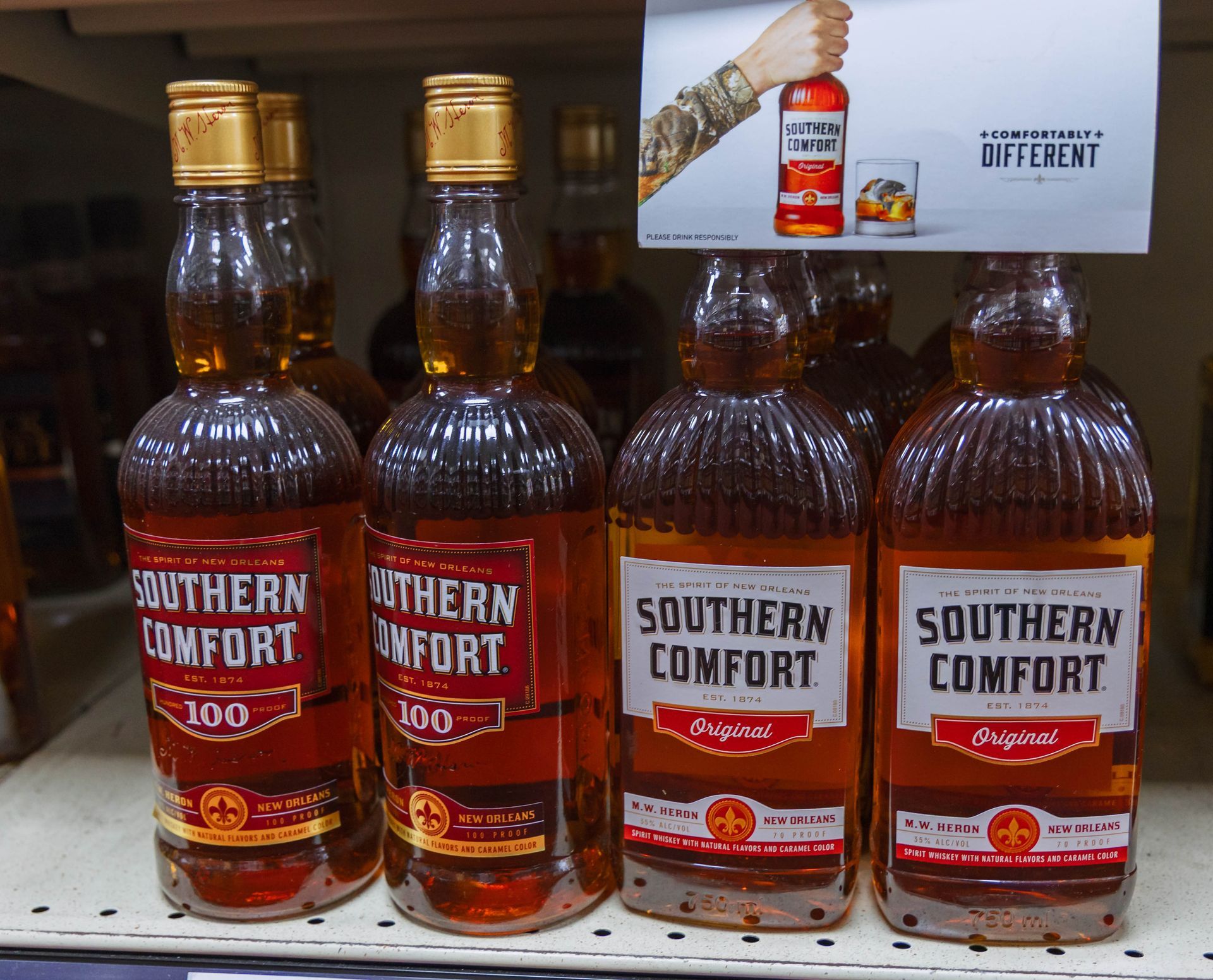 Bottles of Southern Comfort liquor on a shelf, in a store, featuring a promotional sign.