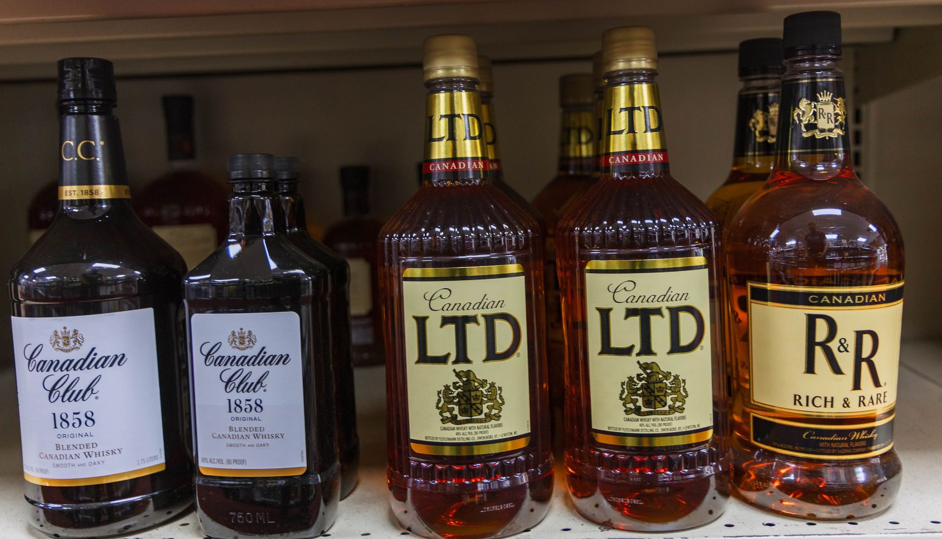 Bottles of liquor on a shelf: Canadian Club and LTD brands, amber liquids, gold and white labels.