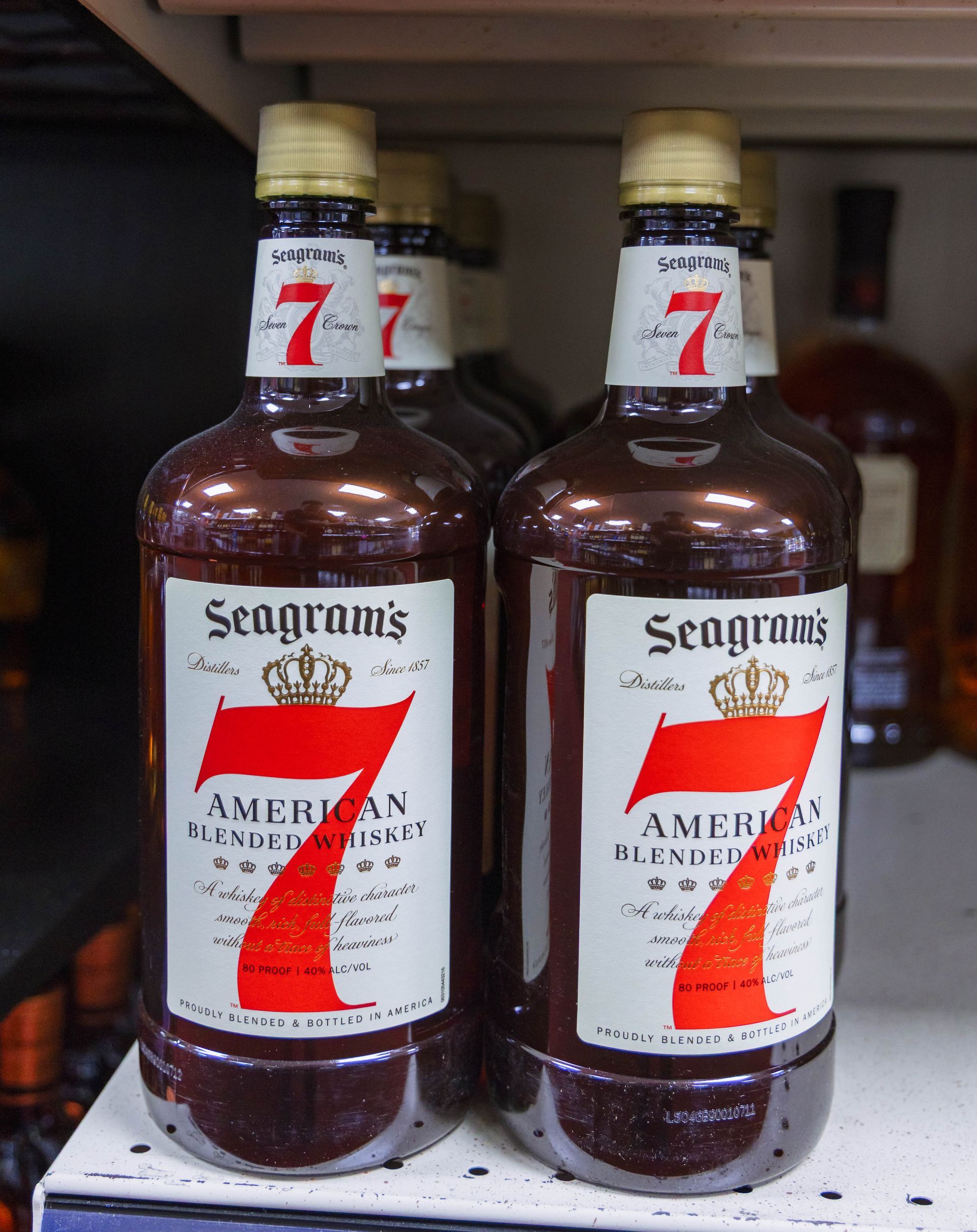 Bottles of Seagram's 7 Crown American Blended Whiskey, dark brown liquid, white and red labels on shelf.