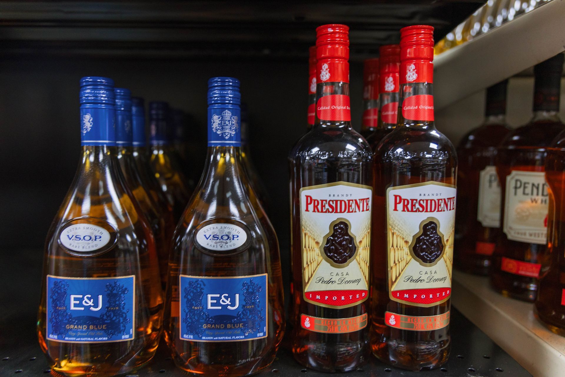 Bottles of liquor on shelves: E&J brandy with blue labels, Presidente brandy with red labels.