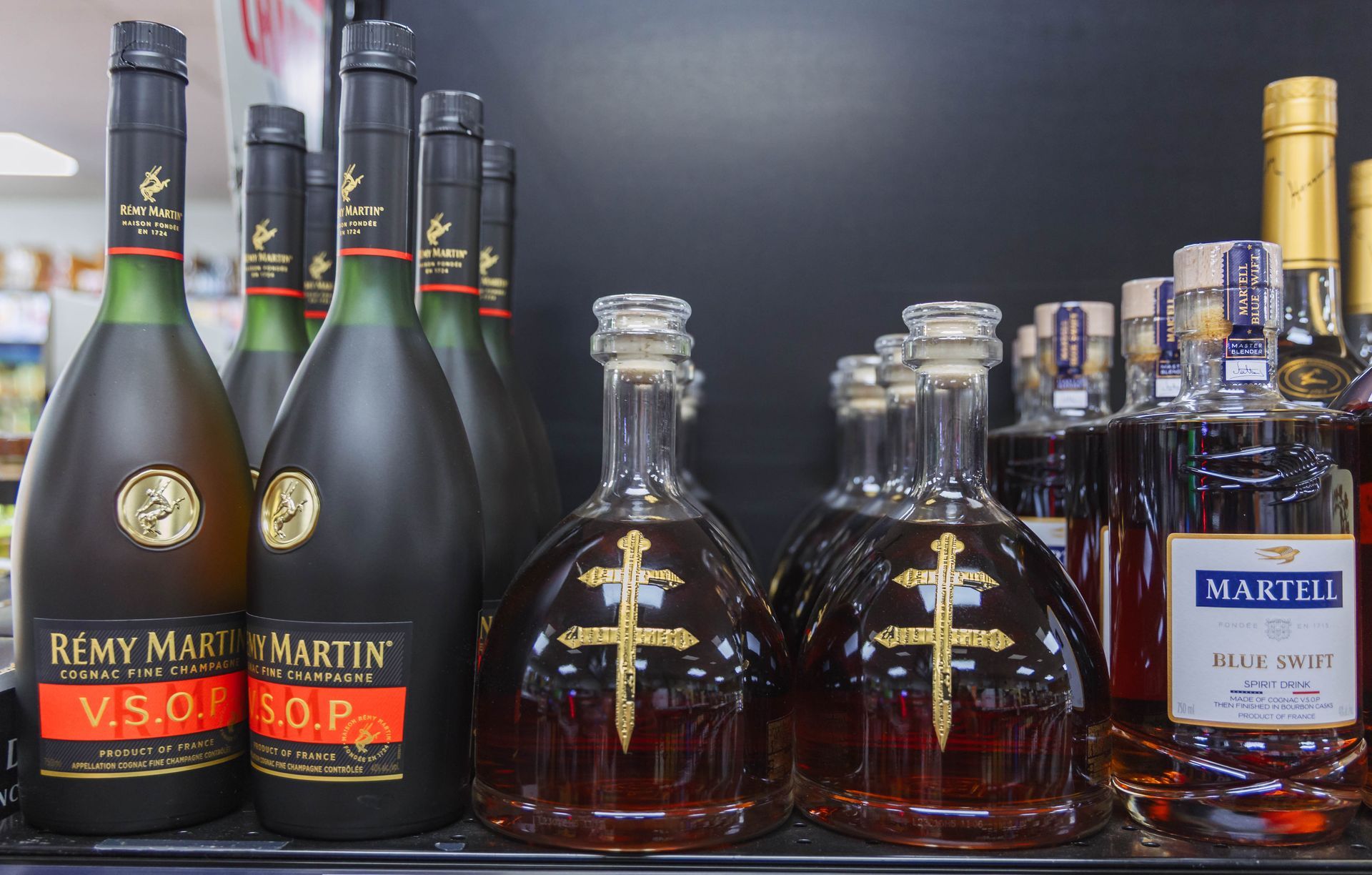 Liquor bottles on a shelf, including Rémy Martin VSOP and bottles with a gold cross design.
