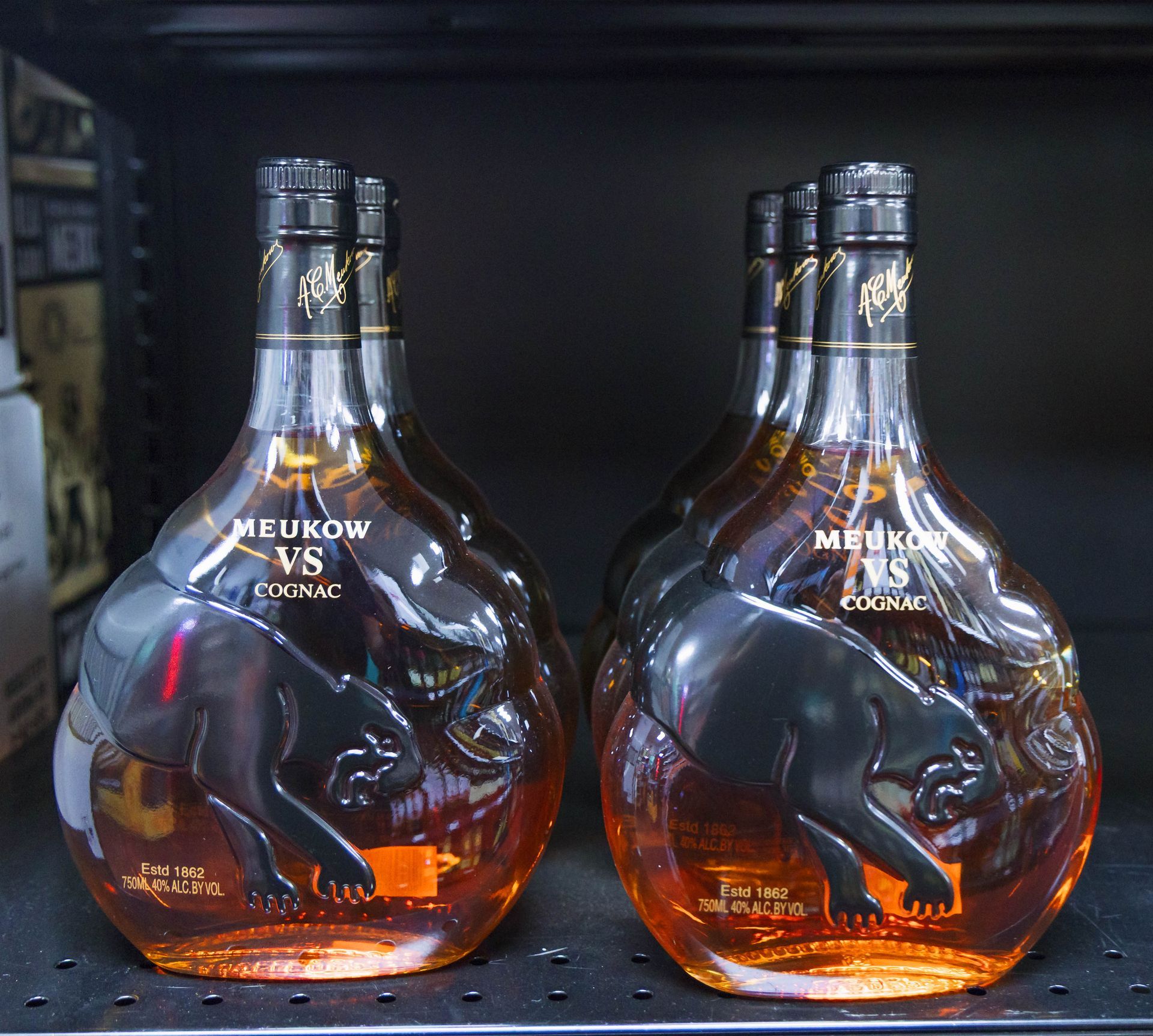 Bottles of Meikow VS Cognac with black panther design, on a shelf.