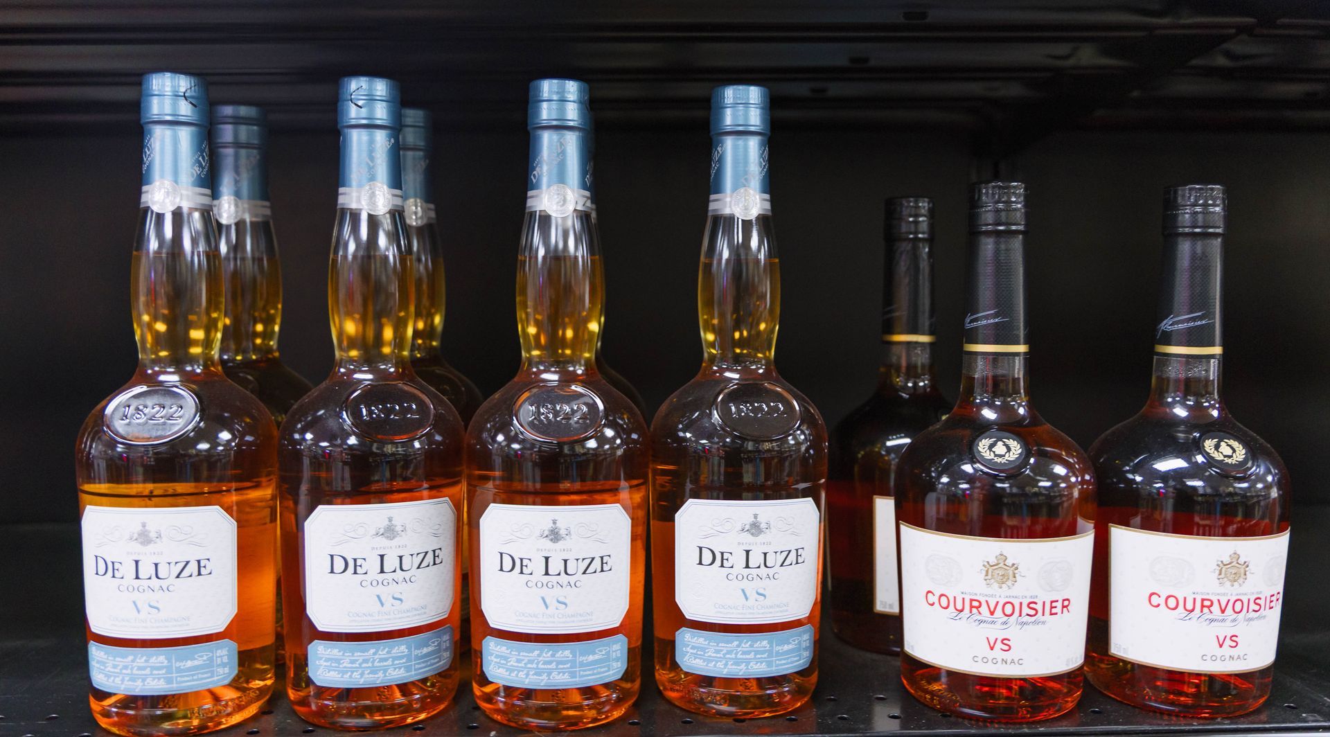 Bottles of liquor on a shelf. Some bottles are amber with blue labels, others are dark with red labels.