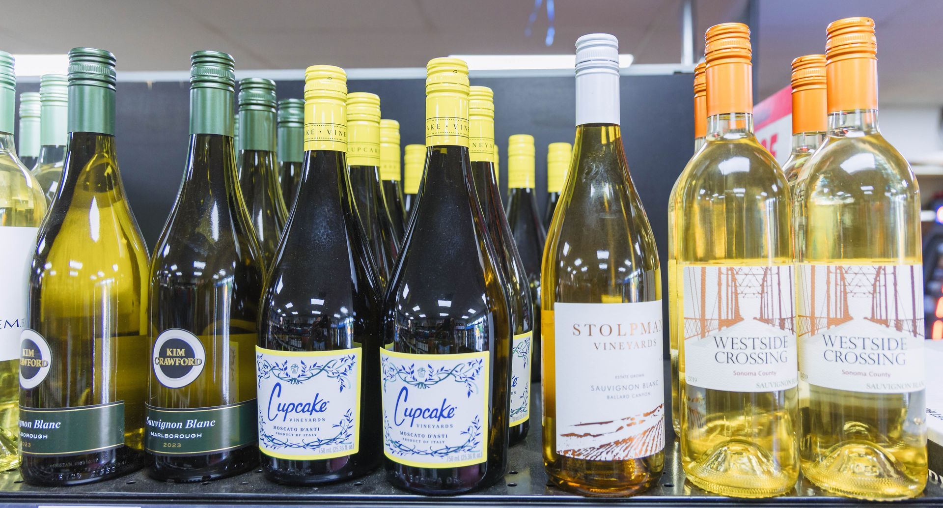 Wine bottles on a store shelf. Various colors of bottles, some with colorful labels, many with yellow, gold, or orange caps.