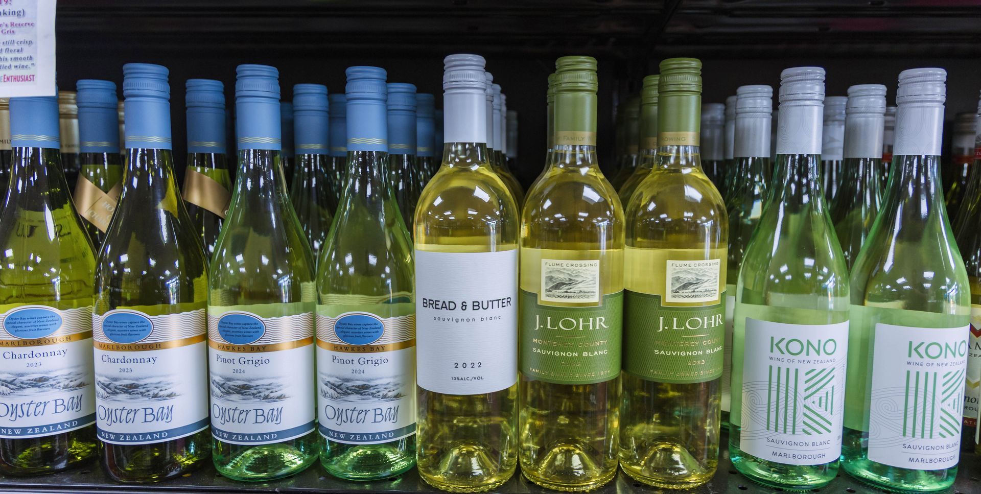 Bottles of white wine in a store, displayed on shelves. The bottles have various labels, colors, and designs.