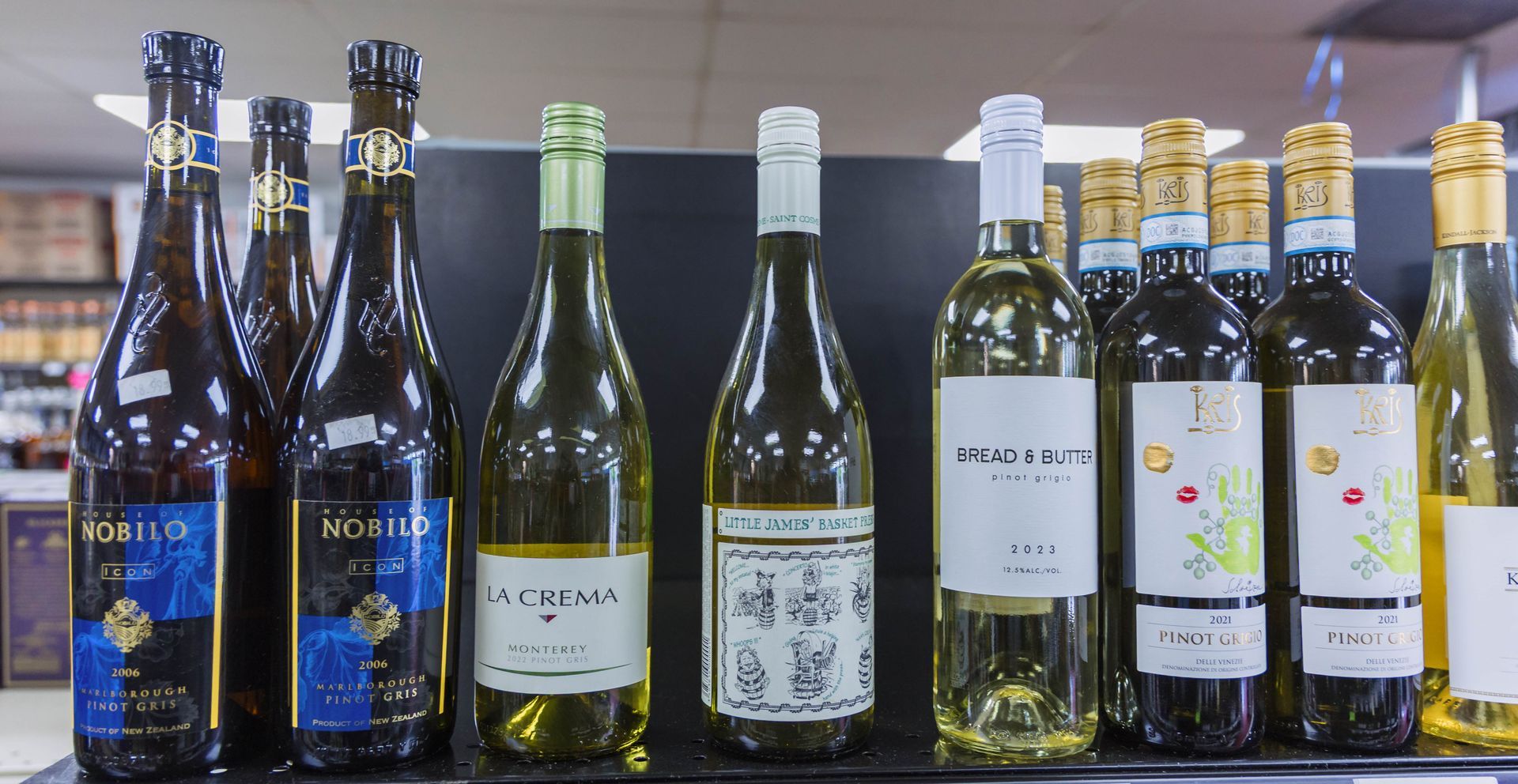 Wine bottles on a shelf; various brands with colorful labels, mostly green, white, and gold.