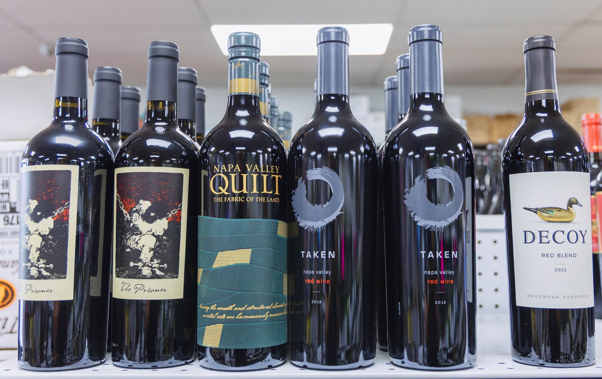 Wine bottles on a shelf, various labels, dark bottles with dark red wine, shop setting.