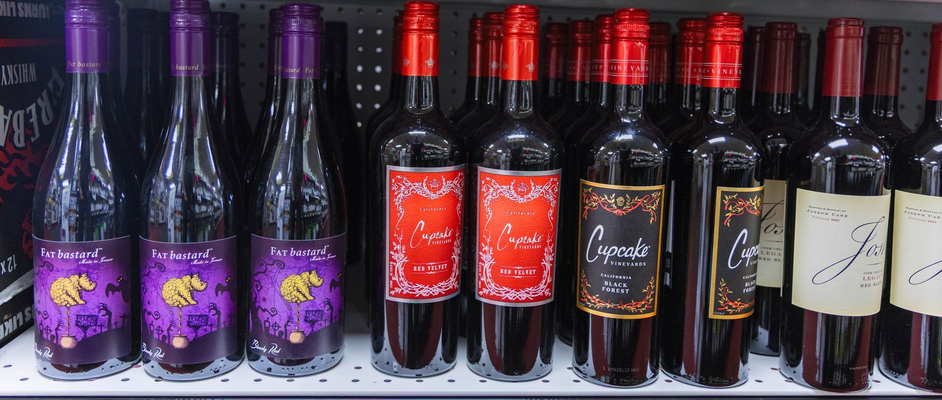 Bottles of wine on a shelf. Some have purple labels, others red and black with gold trim.