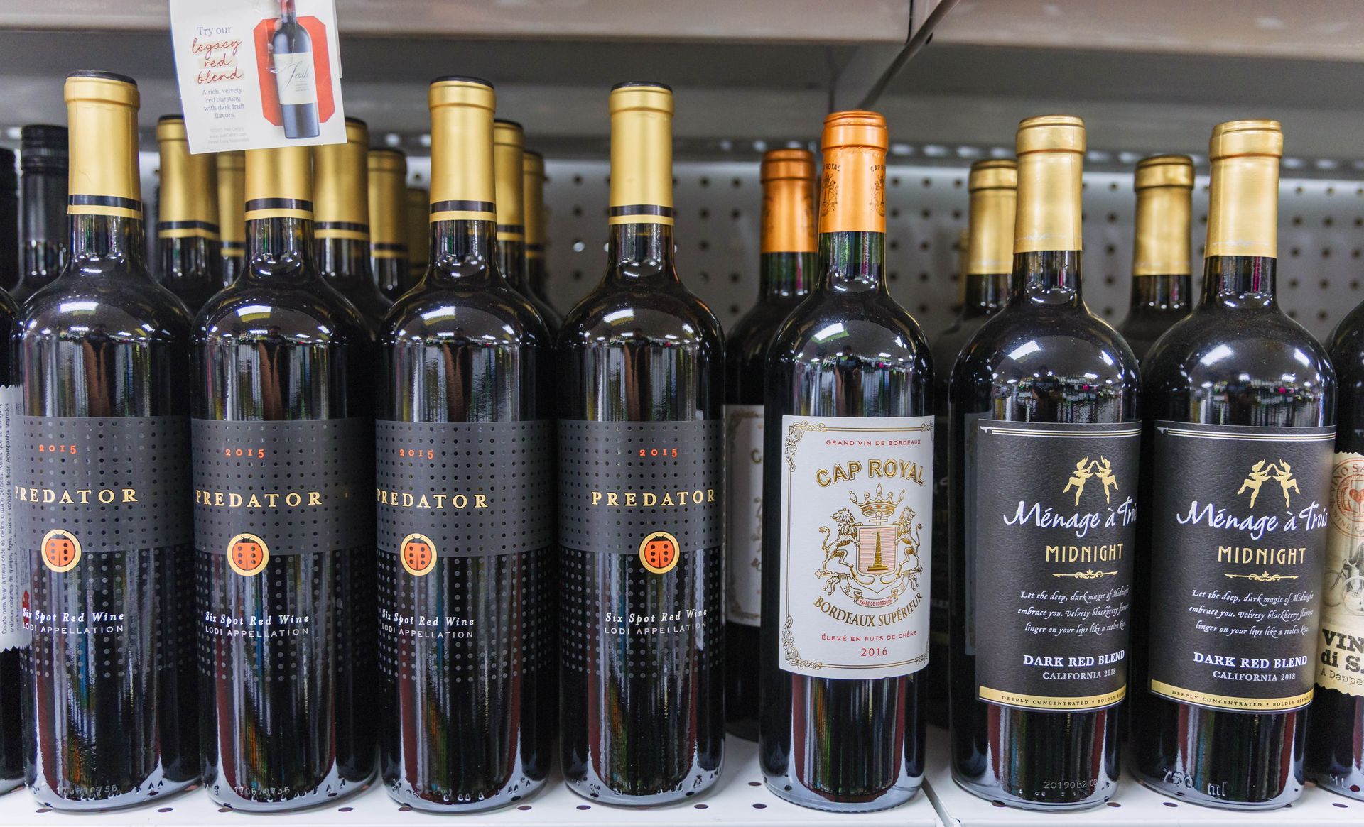 Wine bottles on a shelf, mostly dark bottles with gold tops and labels.