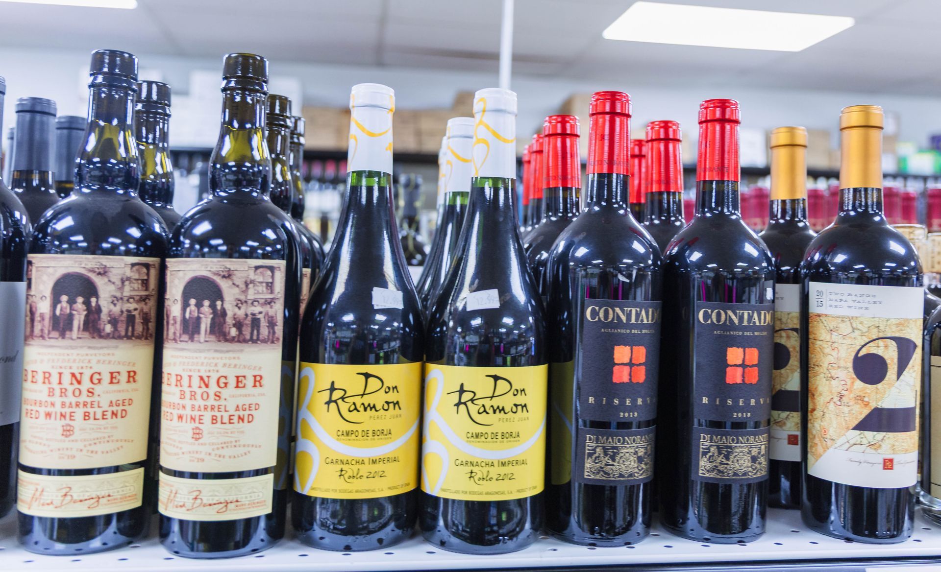 Wine bottles on a store shelf with various labels, including red and yellow, in a brightly lit setting.